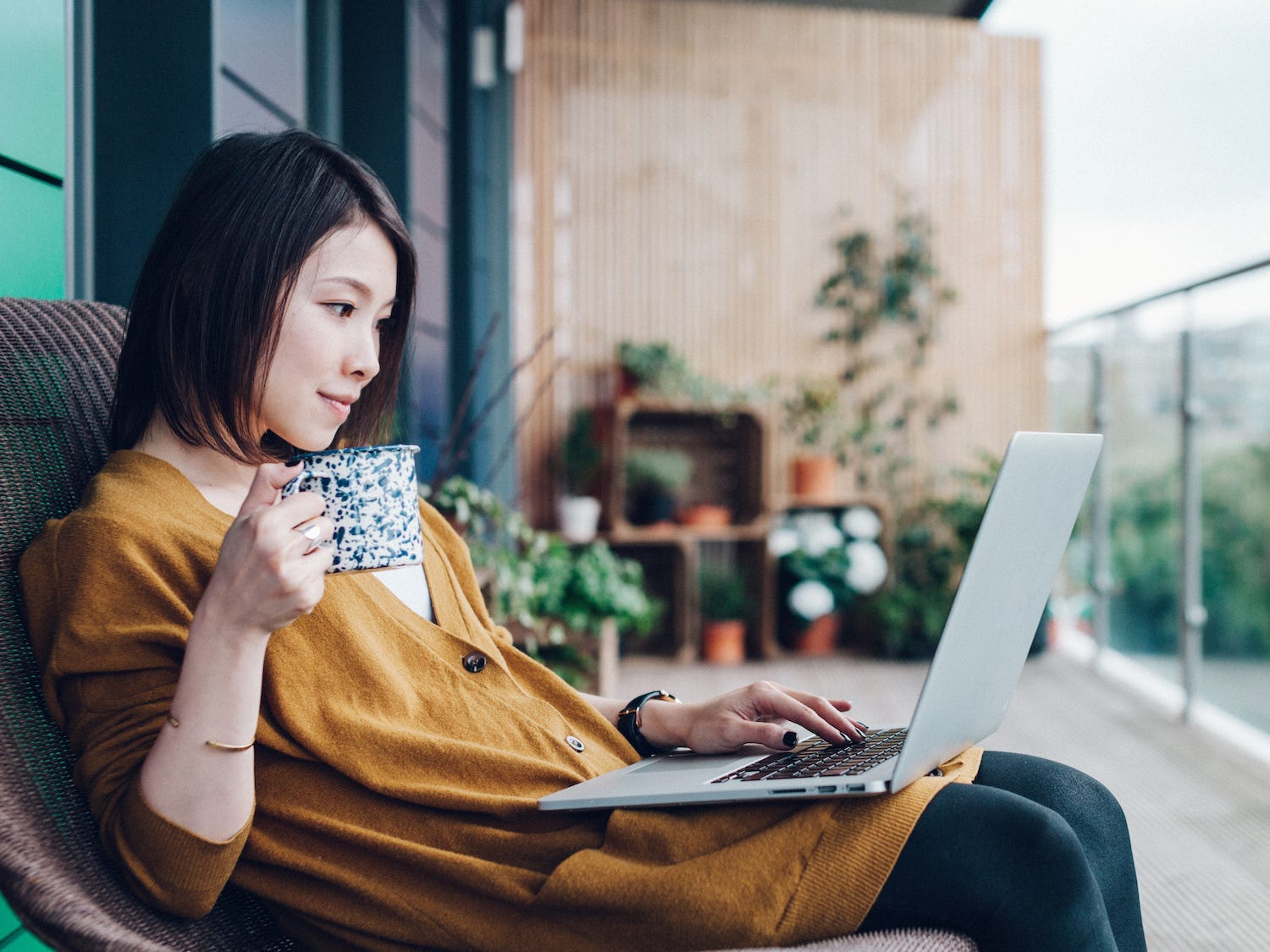 a woman sitting on a balcony looking at a laptop