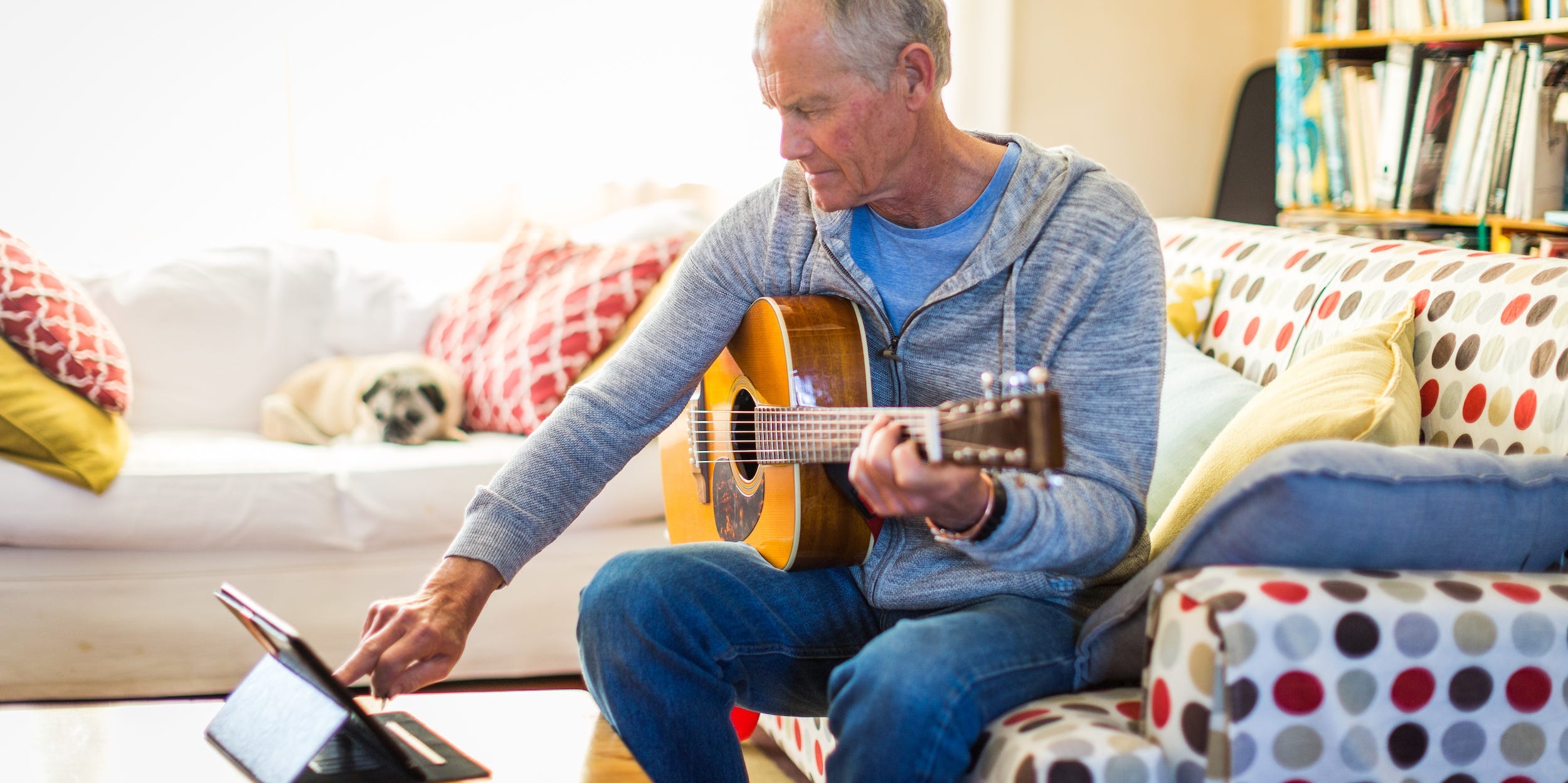 senior man watching guitar video tutorial at home on tablet with guitar in hand