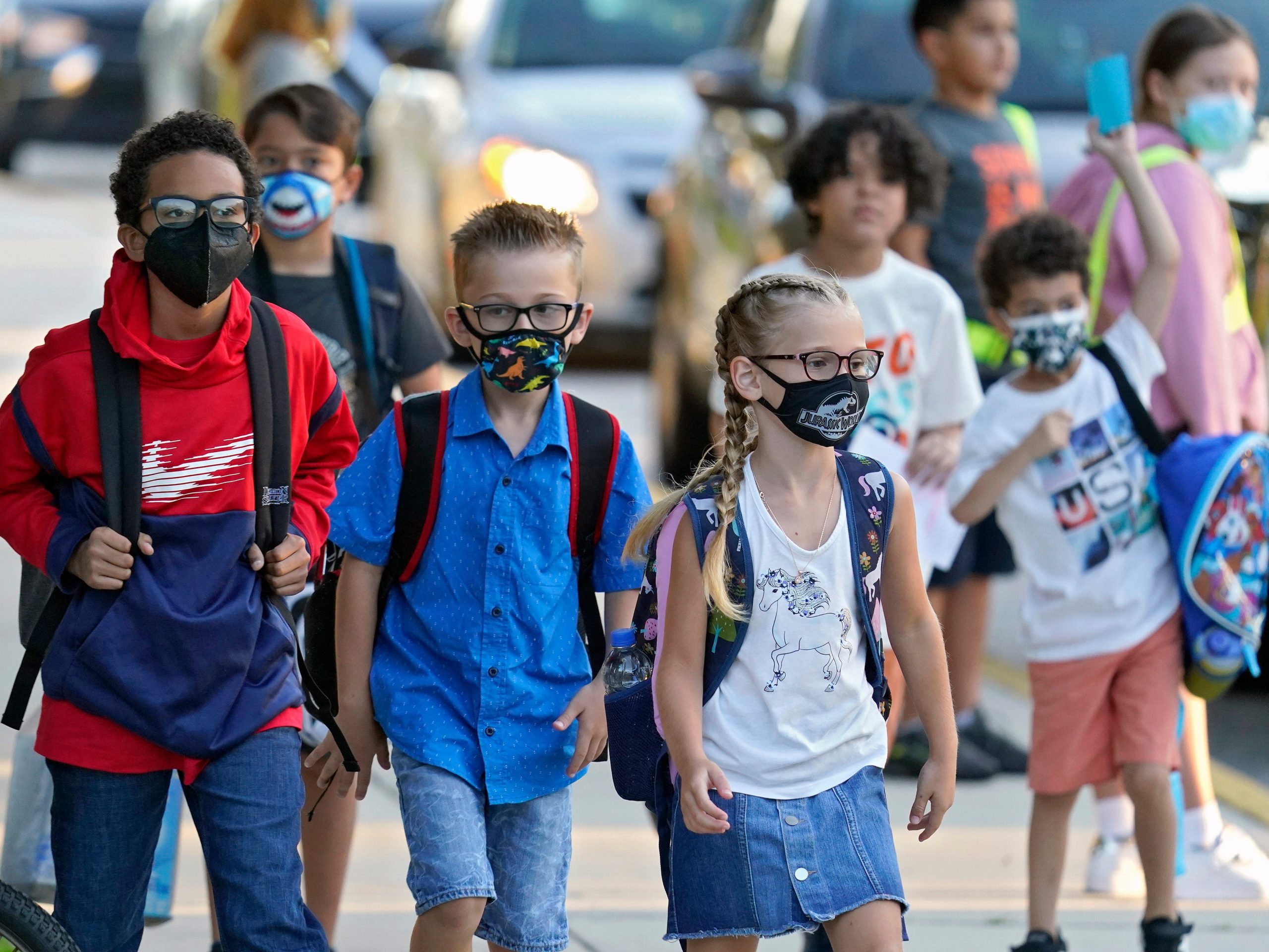 A group of kids wearing masks and backpacks walk toward their classrooms.