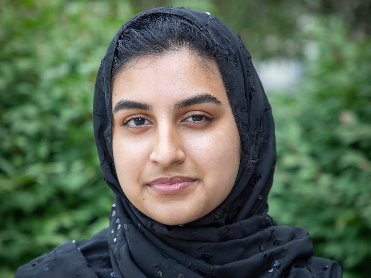 A young Muslim American woman smiling and wearing a black hijab.