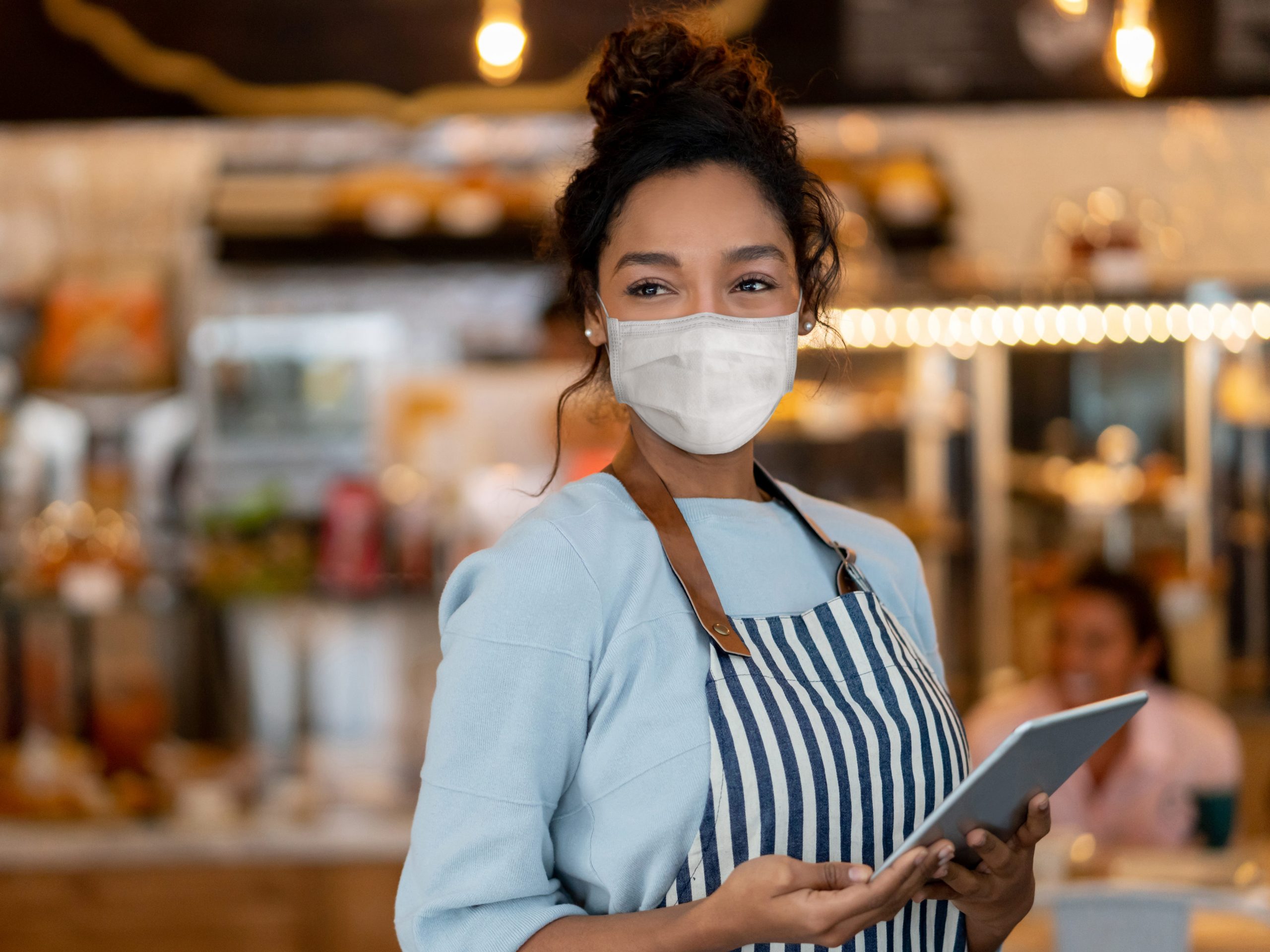 A restaurant worker wears a facemark while holding a tablet to take customer orders.