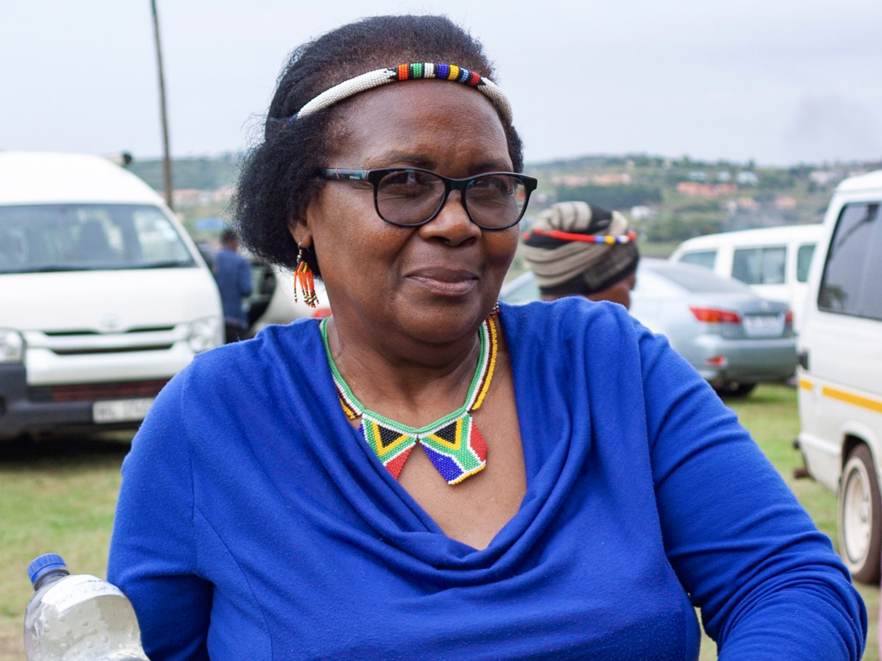 Fikile Ntshangase woman in blue with colorful necklace headband holding water bottles
