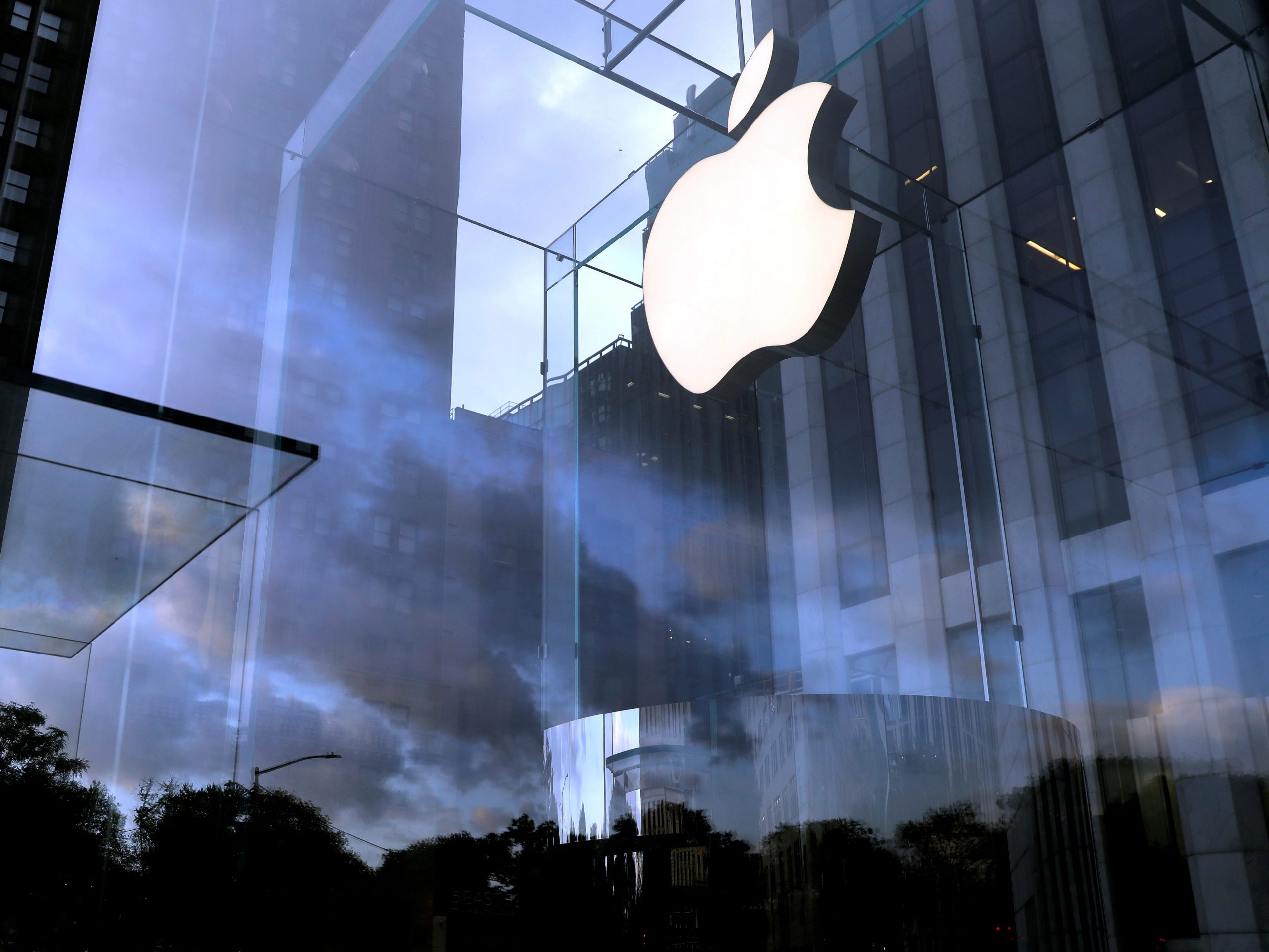 A cloudy sky behind a brightly lit Apple logo in a Manhattan store