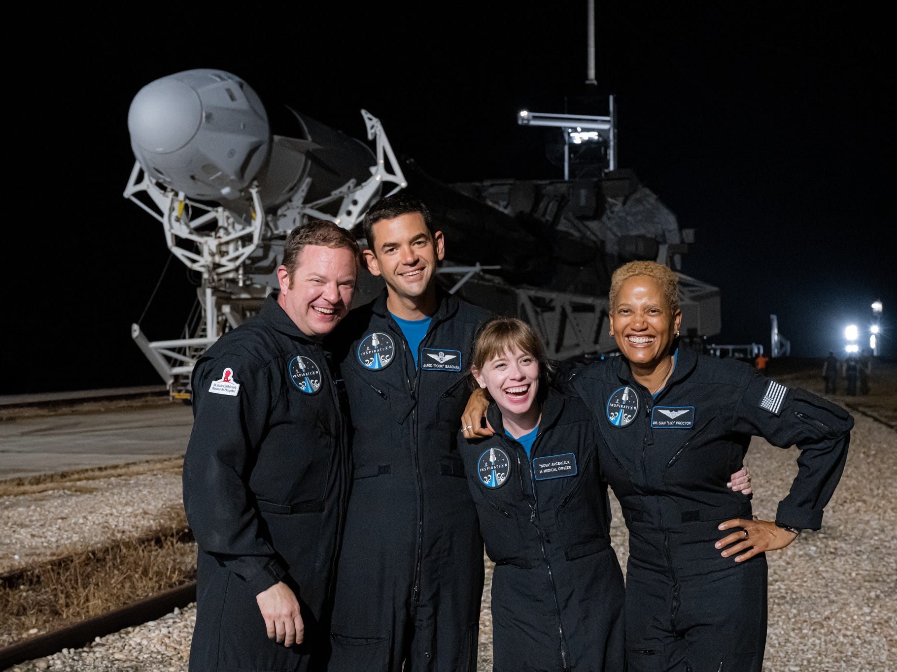 inspiration4 crew poses in front of falcon 9 rocket that's laying sideways on runway at night