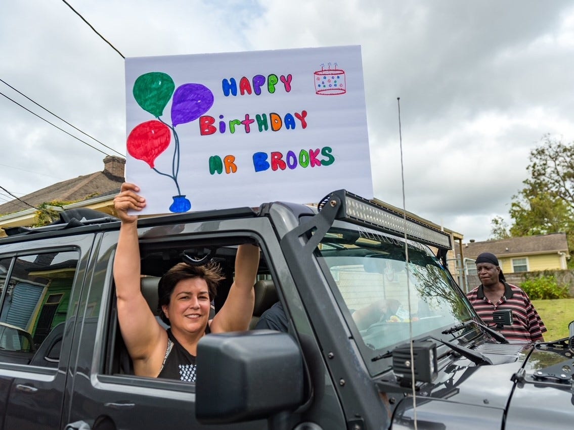 A person holds a sign reading "Happy birthday Mr. Brooks" out of a car window.