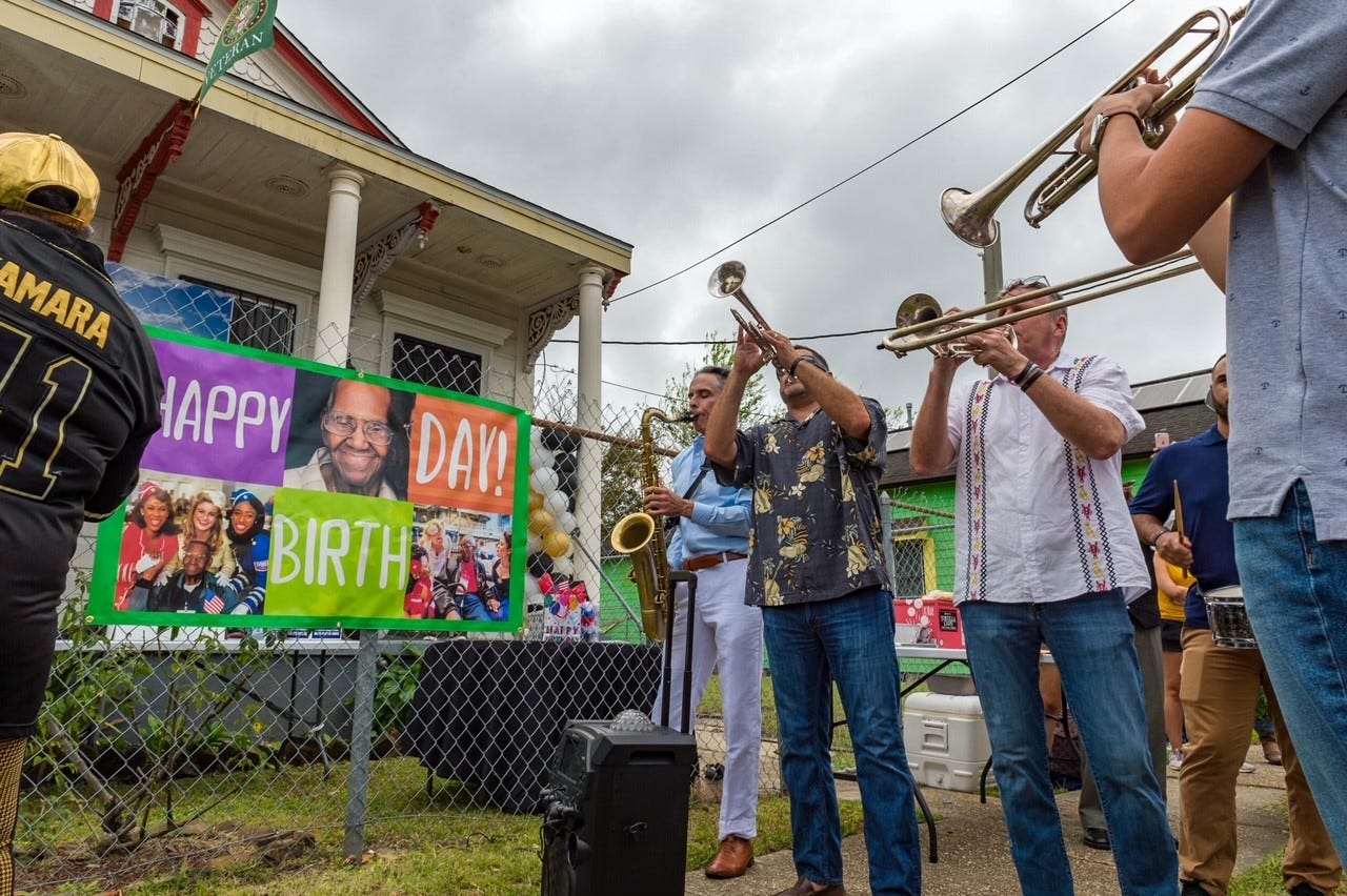 Musicians play outside the home of Lawrence Brooks next to a sign reading "Happy birthday!"