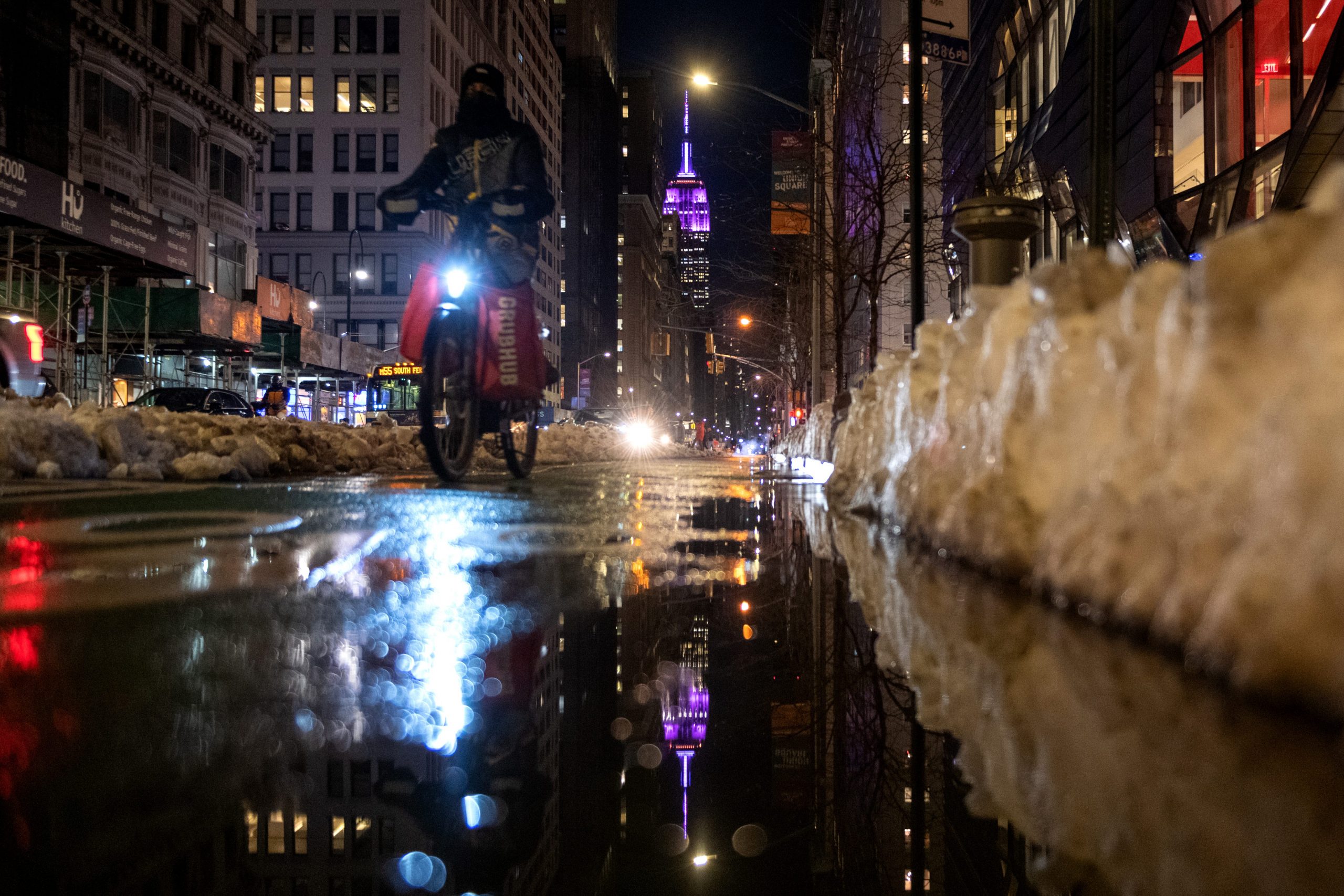 A Grubhub delivery driver rides near the Empire State Building lit up in purple in honor of World Cancer Day on February 04, 2021 in New York City.