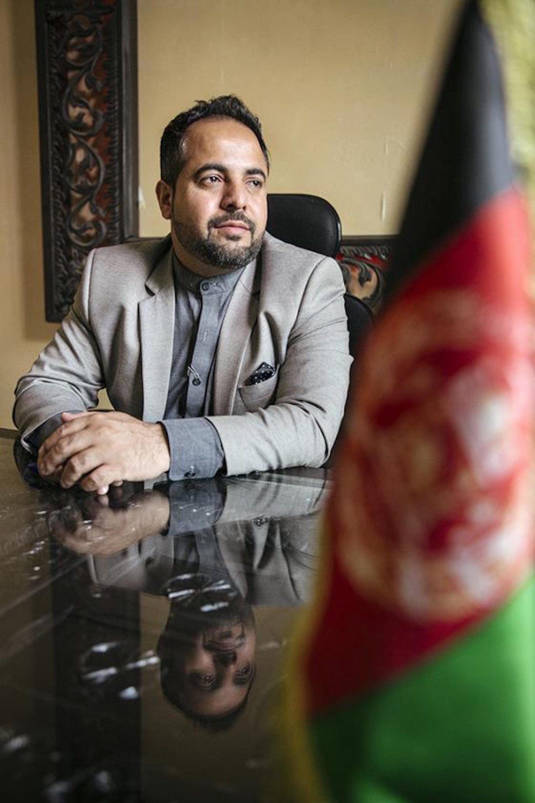 Hamid Samar sitting at a table, with the flag of Afghanistan in the foreground.