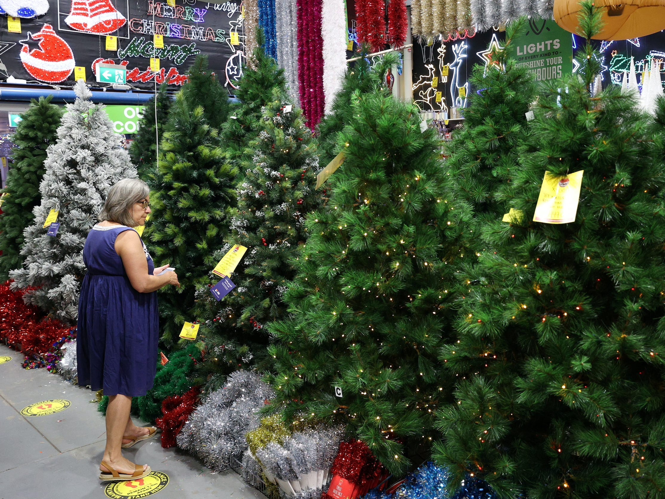 Woman stands in front of display of artificial Christmas trees