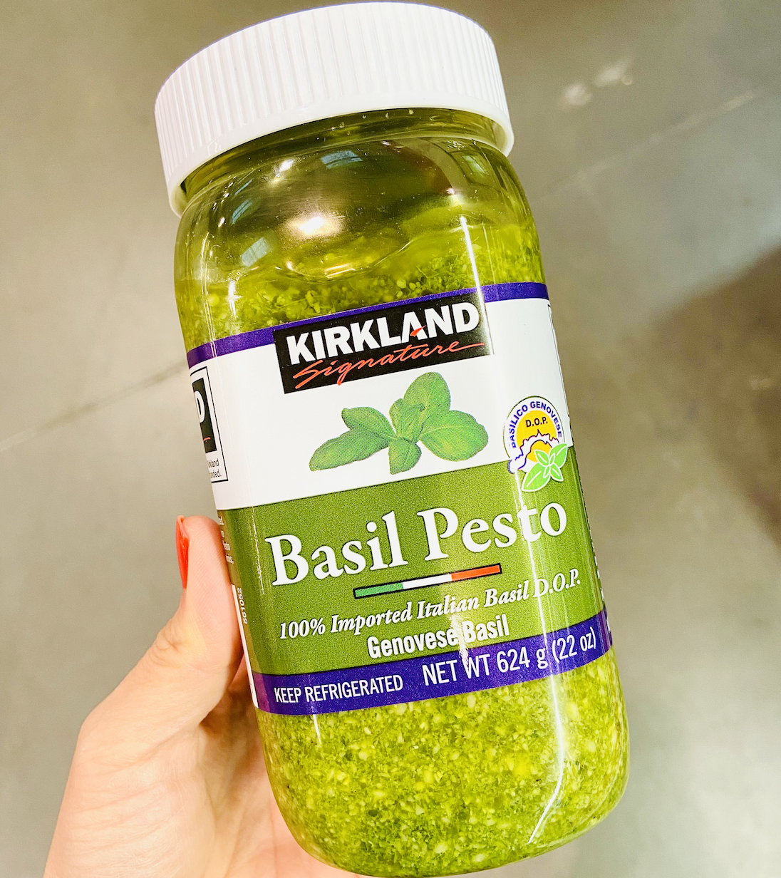 Hand holding a jar of bright green pesto from costco