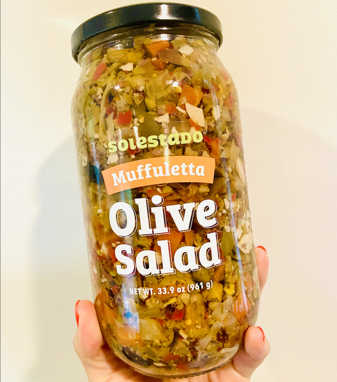 A hand holding a jar of olive salad, which is brown and red