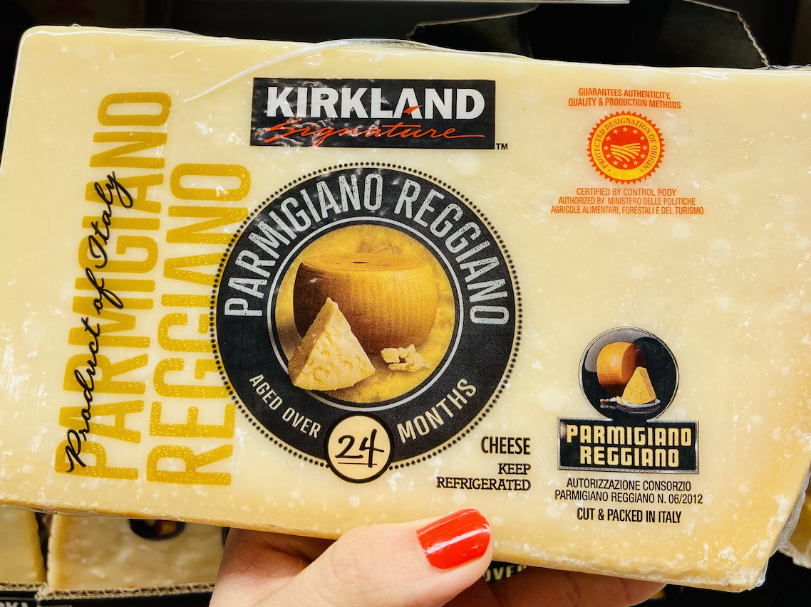 A hand holding a block of Kirkland parmigiano reggiano in the cheese section