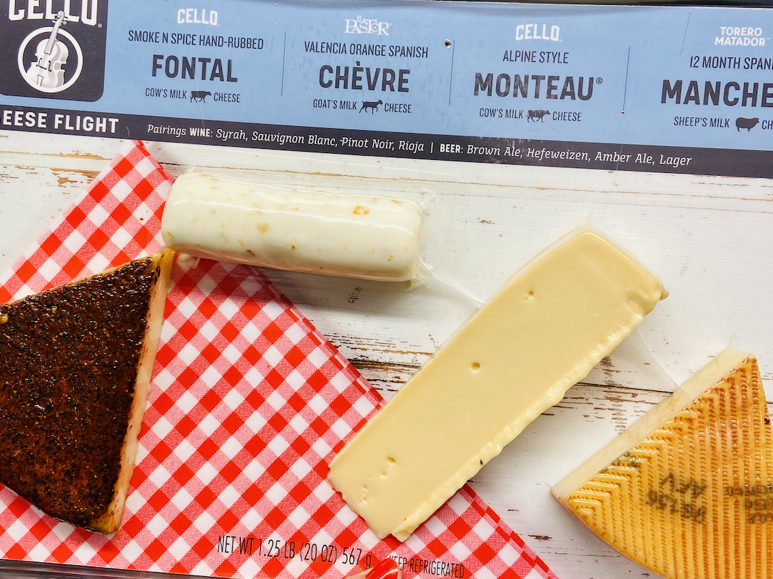Hand holding a red and white package of Costco cheese flight, with four different cheese