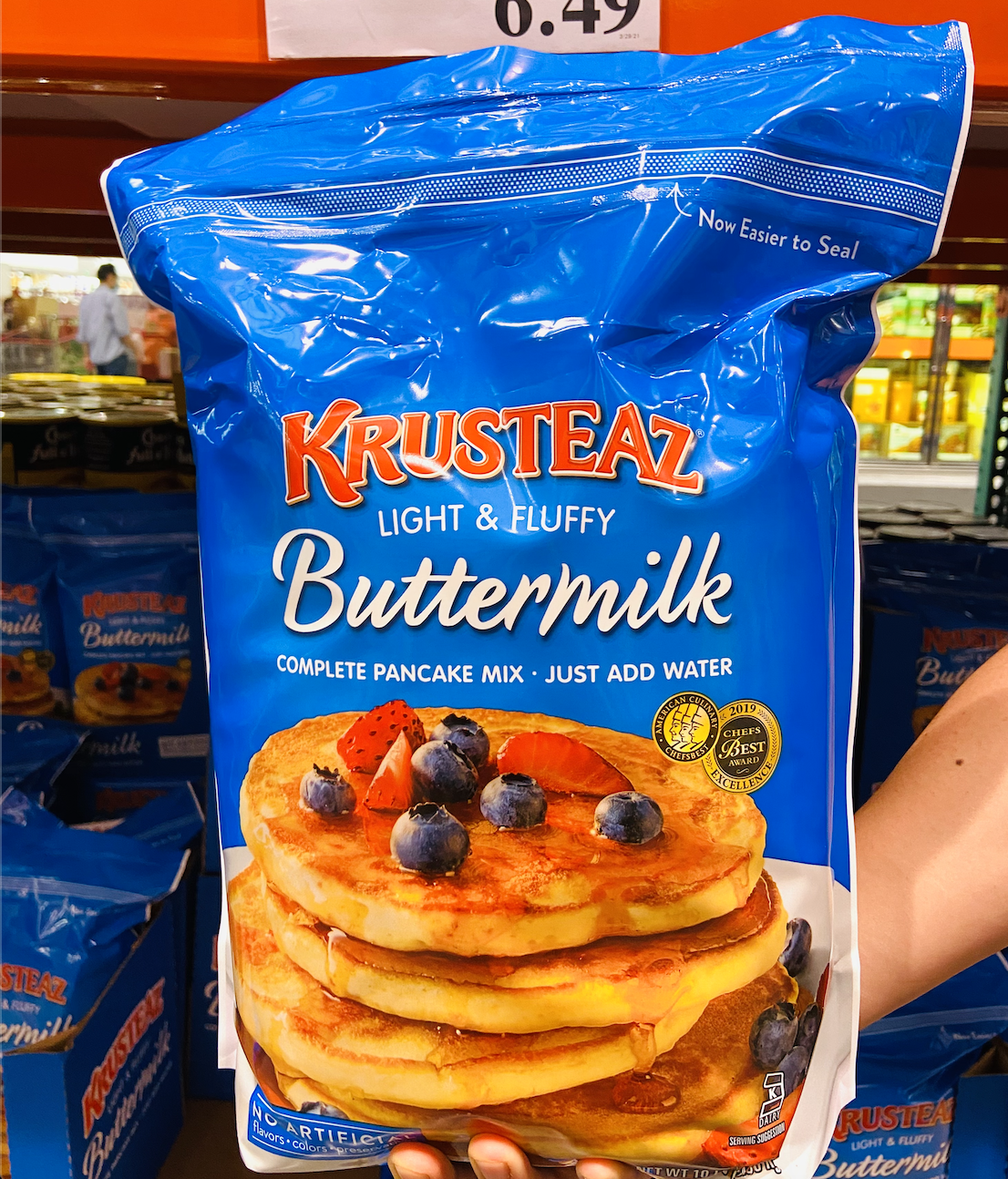 A hand holding the blue bag of Krusteaz buttermilk pancake mix