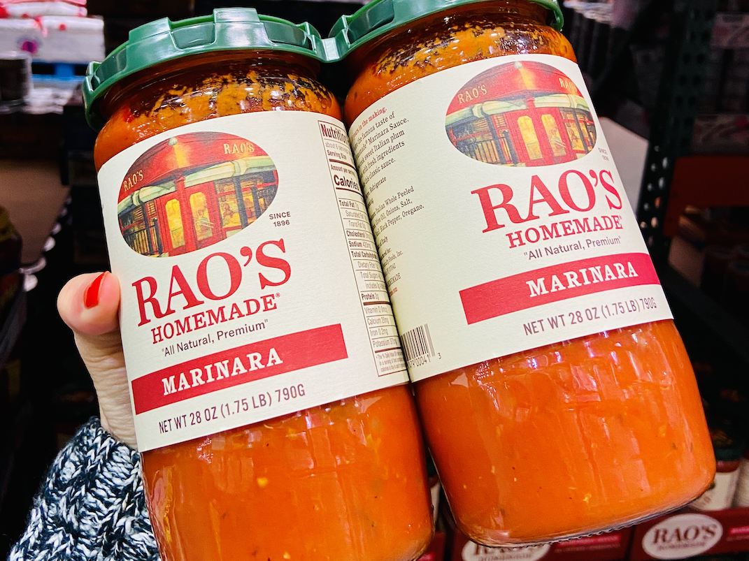 A hand holding a two-pack of Rao's marinara sauce from Costco
