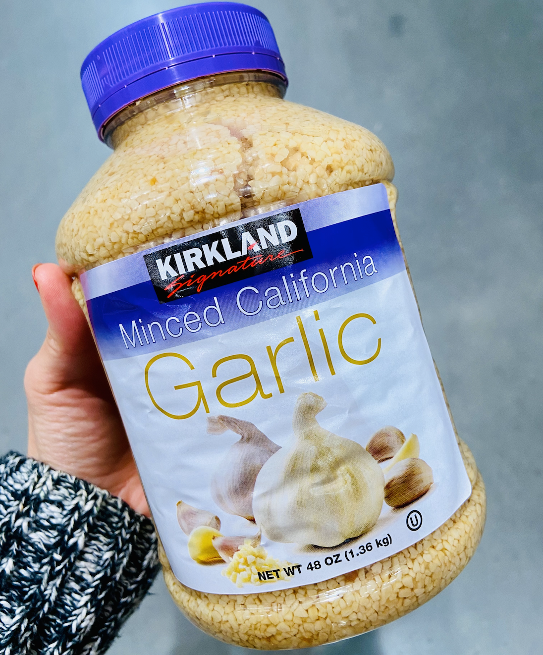 Hand holding a large container of minced garlic from costco