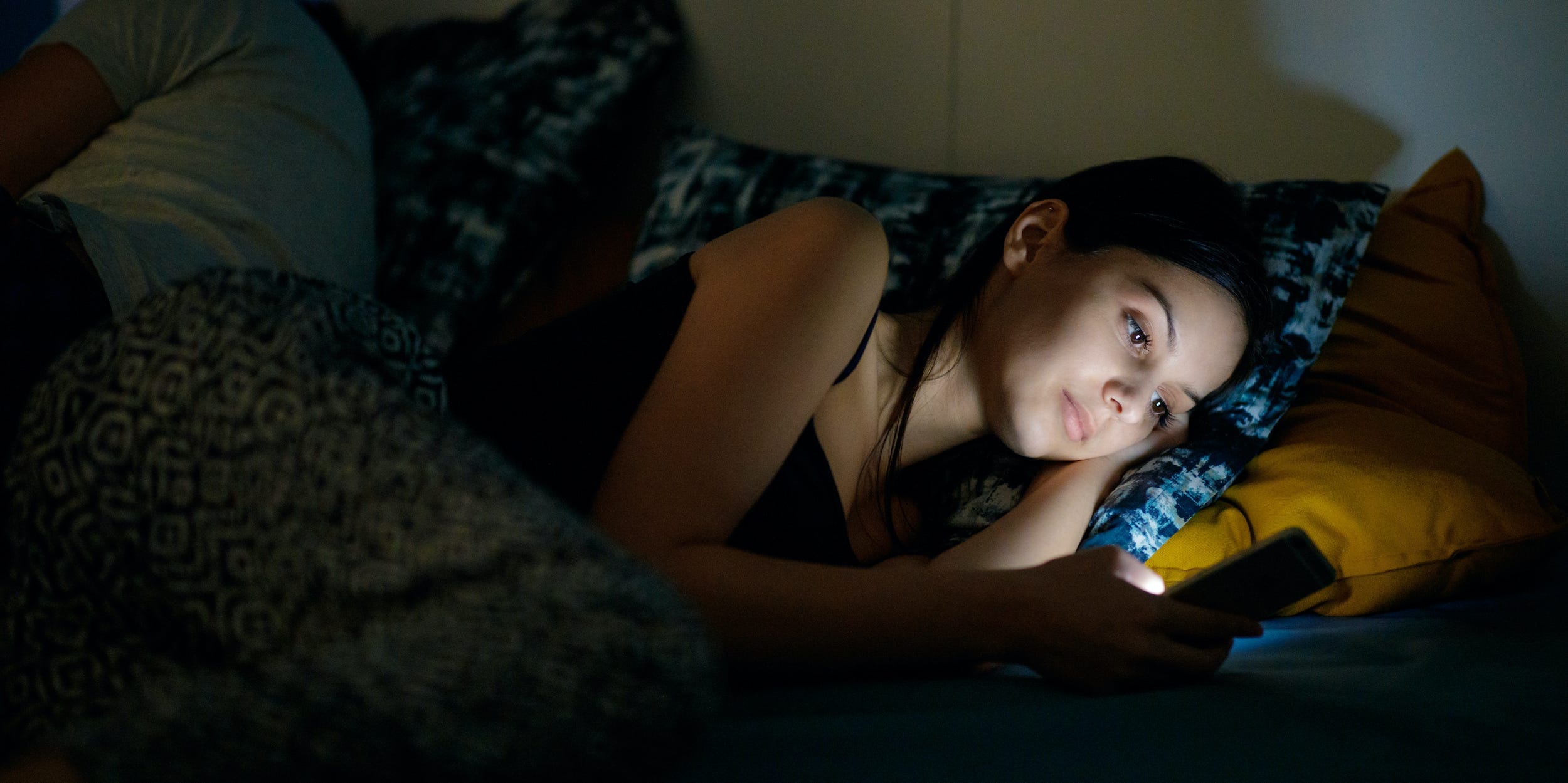 Woman laying in bed looking at phone dark at nighttime