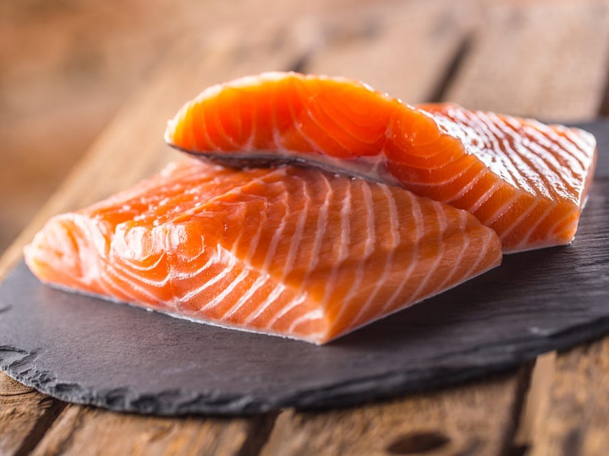 Two pieces of salmon on a wooden table.