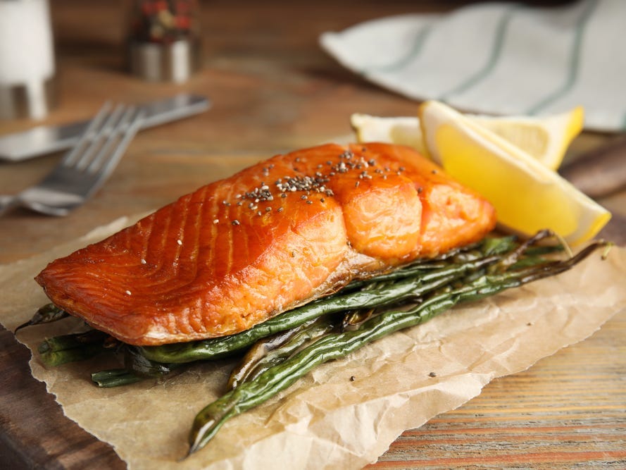 A piece of cooked salmon and vegetables on a wooden table.