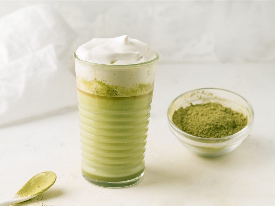 A glass of matcha with a small bowl of matcha powder.