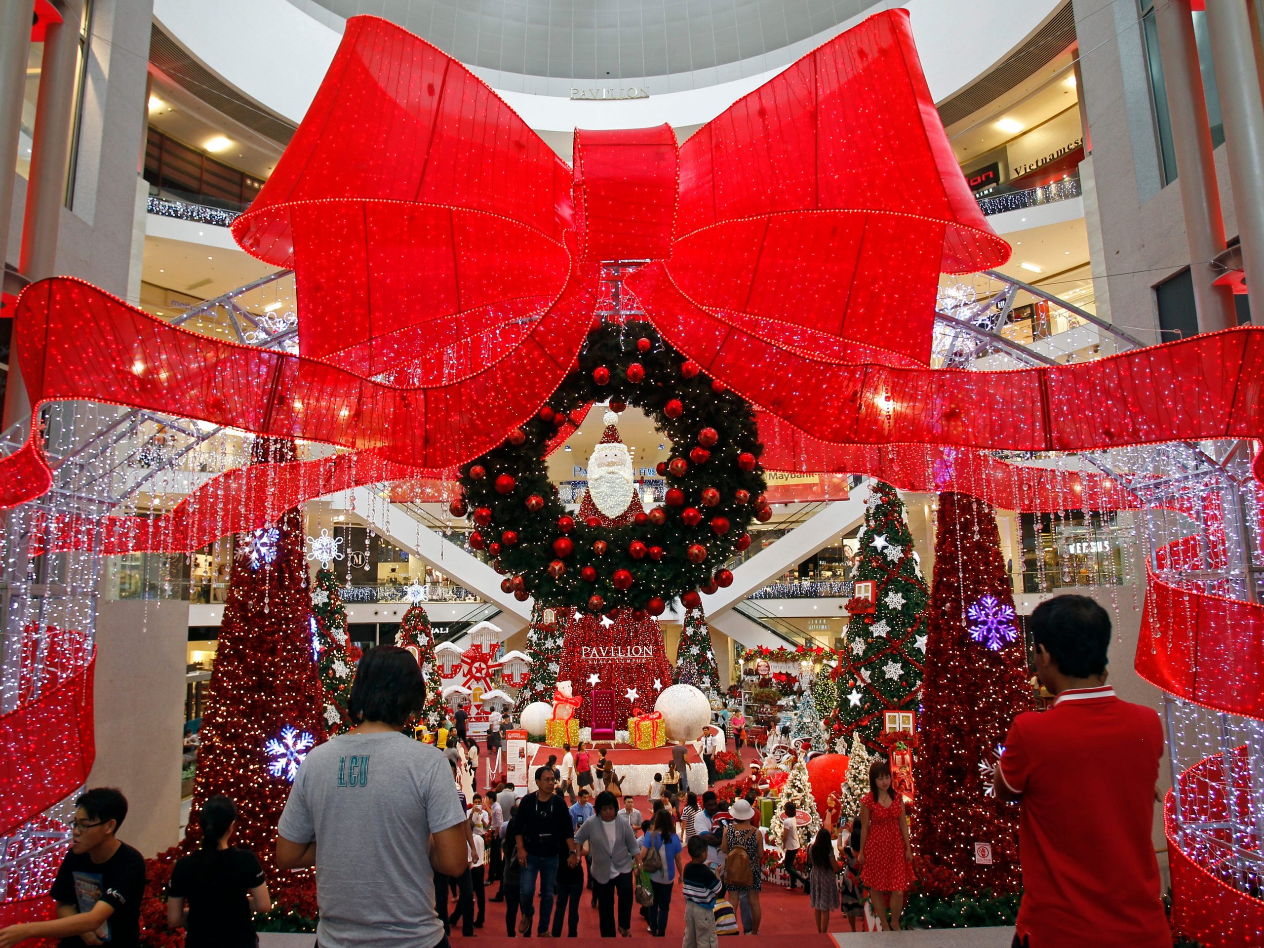 crowds walk by a holiday shopping display with a big red bow and a Christmas wreath