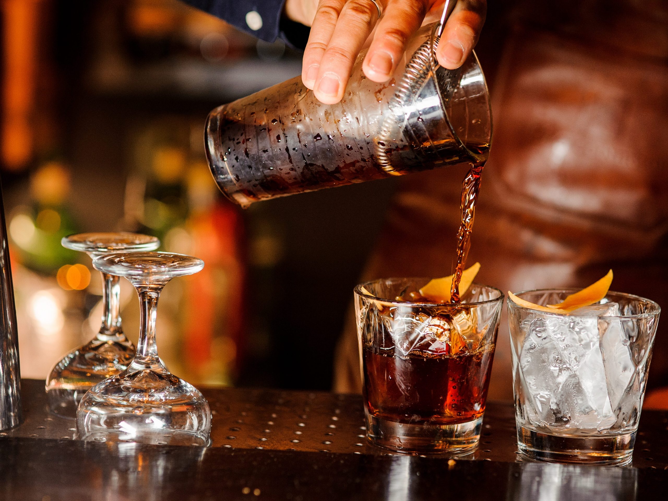 Barman pouring fresh alcoholic drink into the glasses with ice cubes on the bar counter.