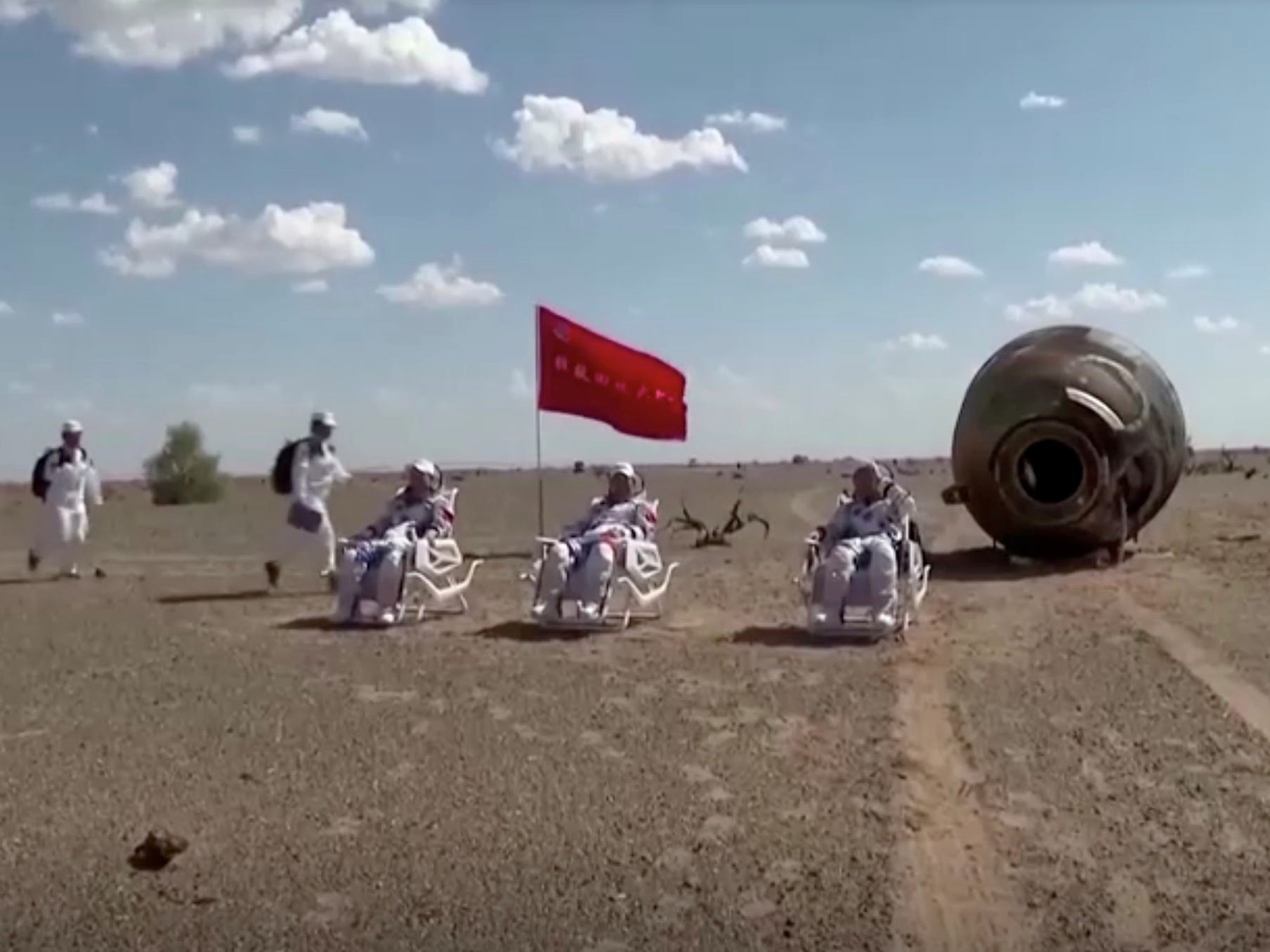 chinese astronauts sit in chairs next to charred spaceship after landing in mongolia desert from space station mission