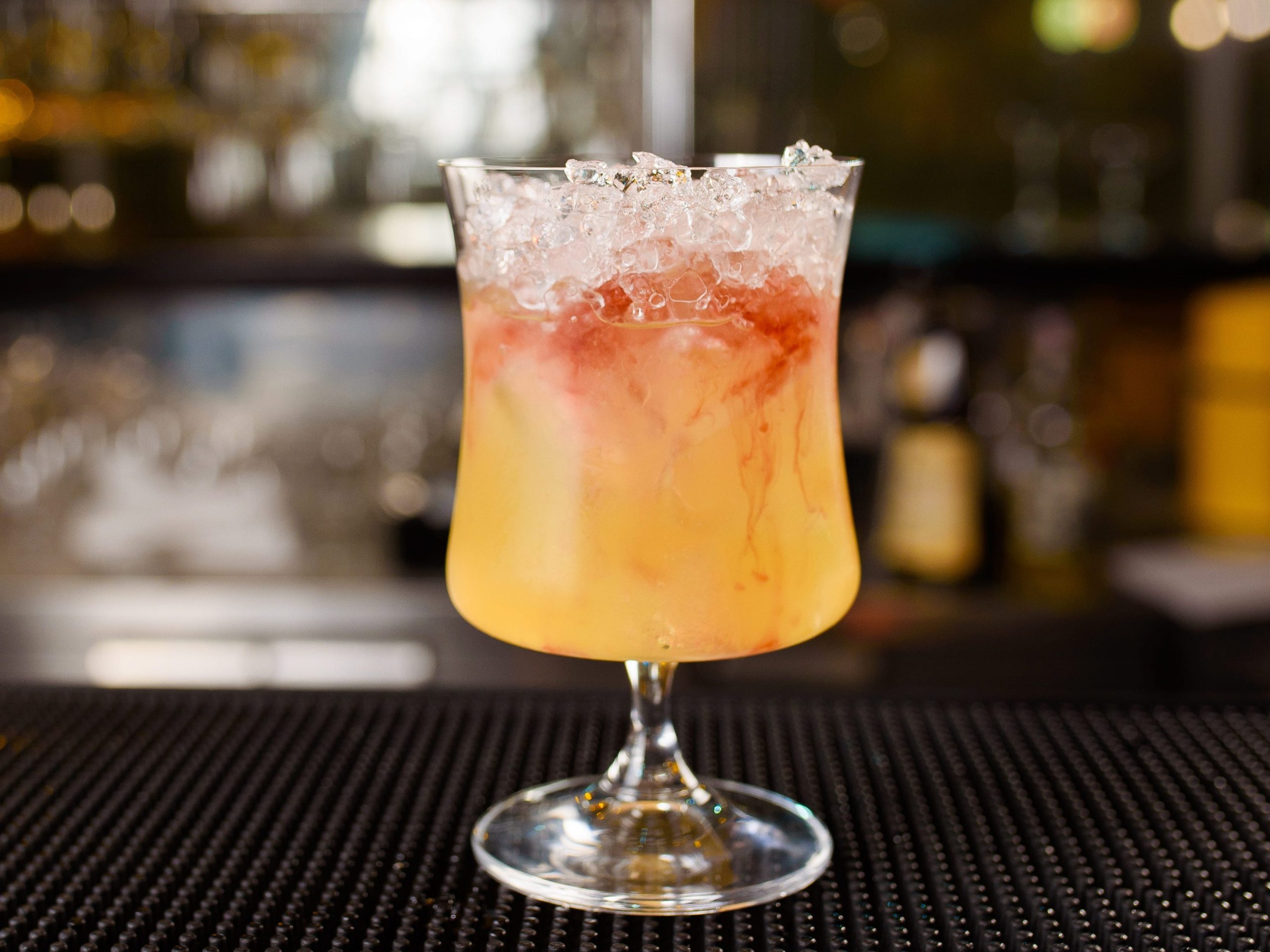 An orange cocktail in a wide glass on a bar.