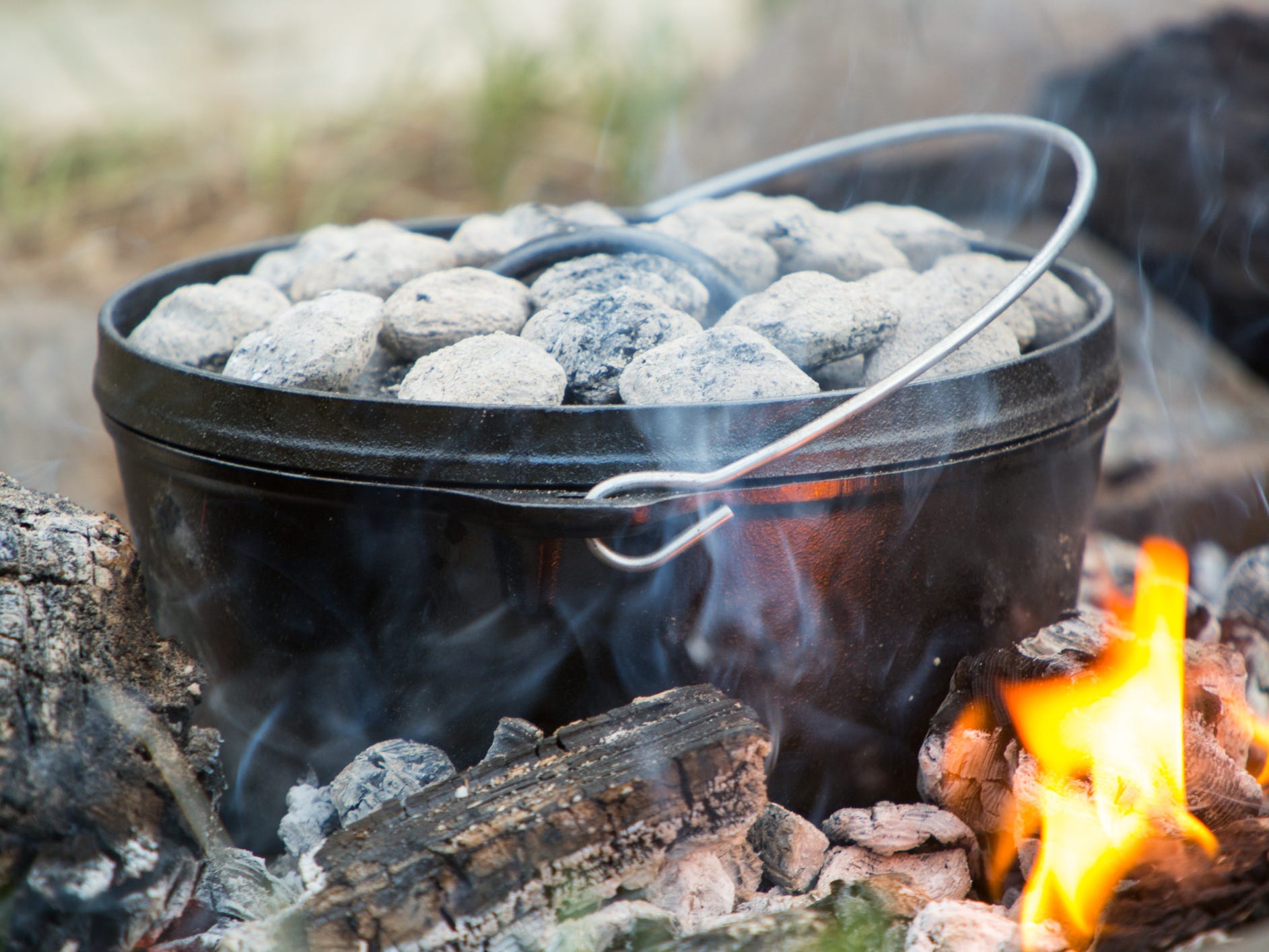 A cast iron Dutch oven cooking over an open fire, topped with charcoal