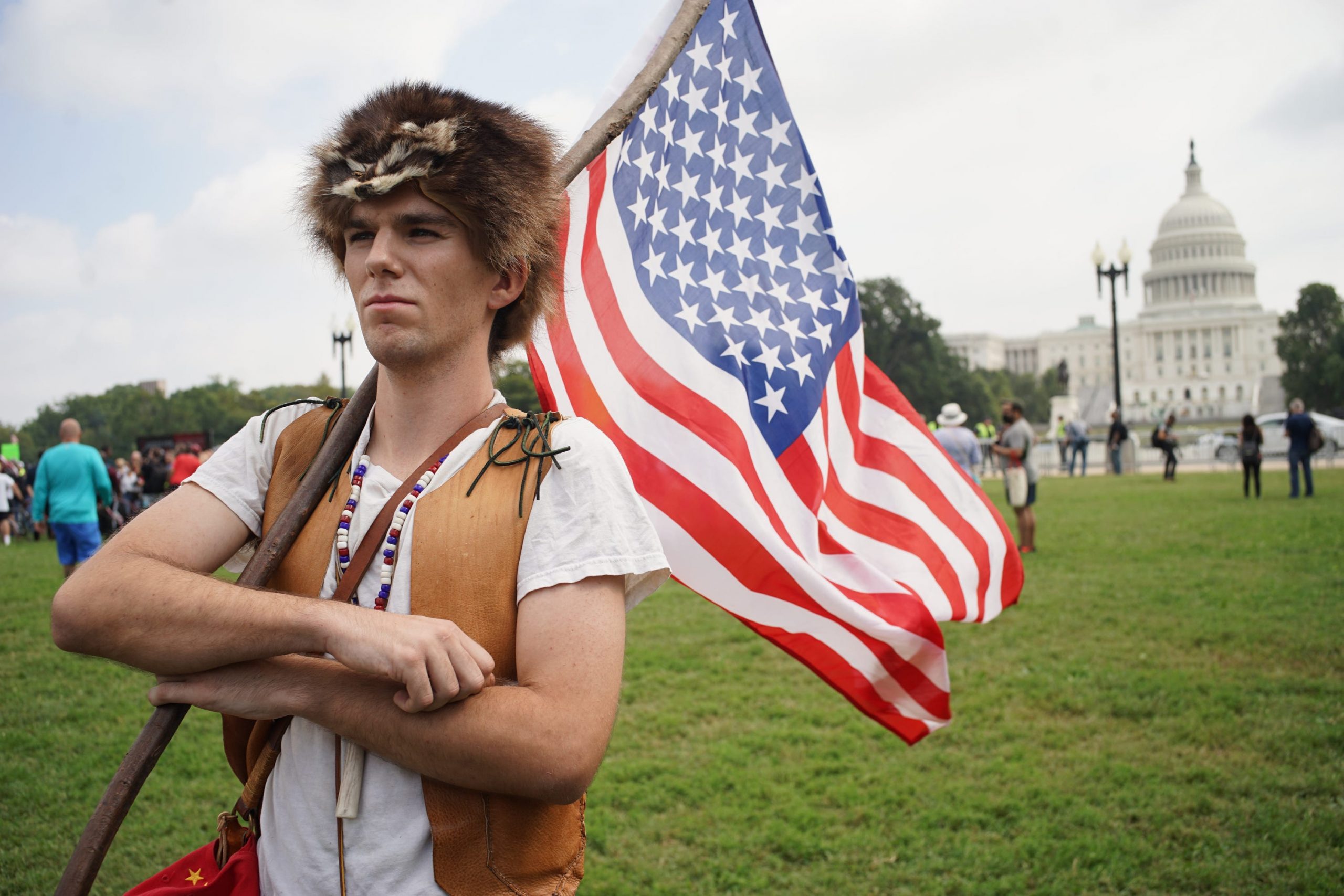A man in a raccoon-fur hat holding am American flag in front of the US Capitol.