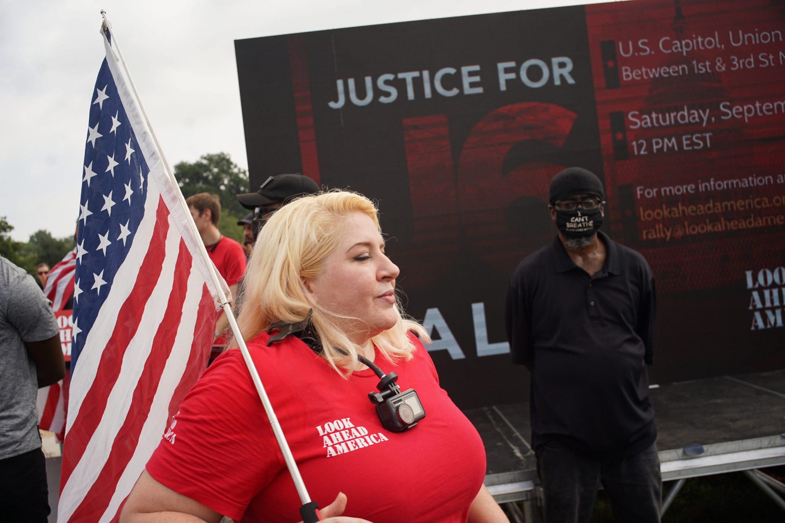 A protester holds an American flag as a security person stands behind her.
