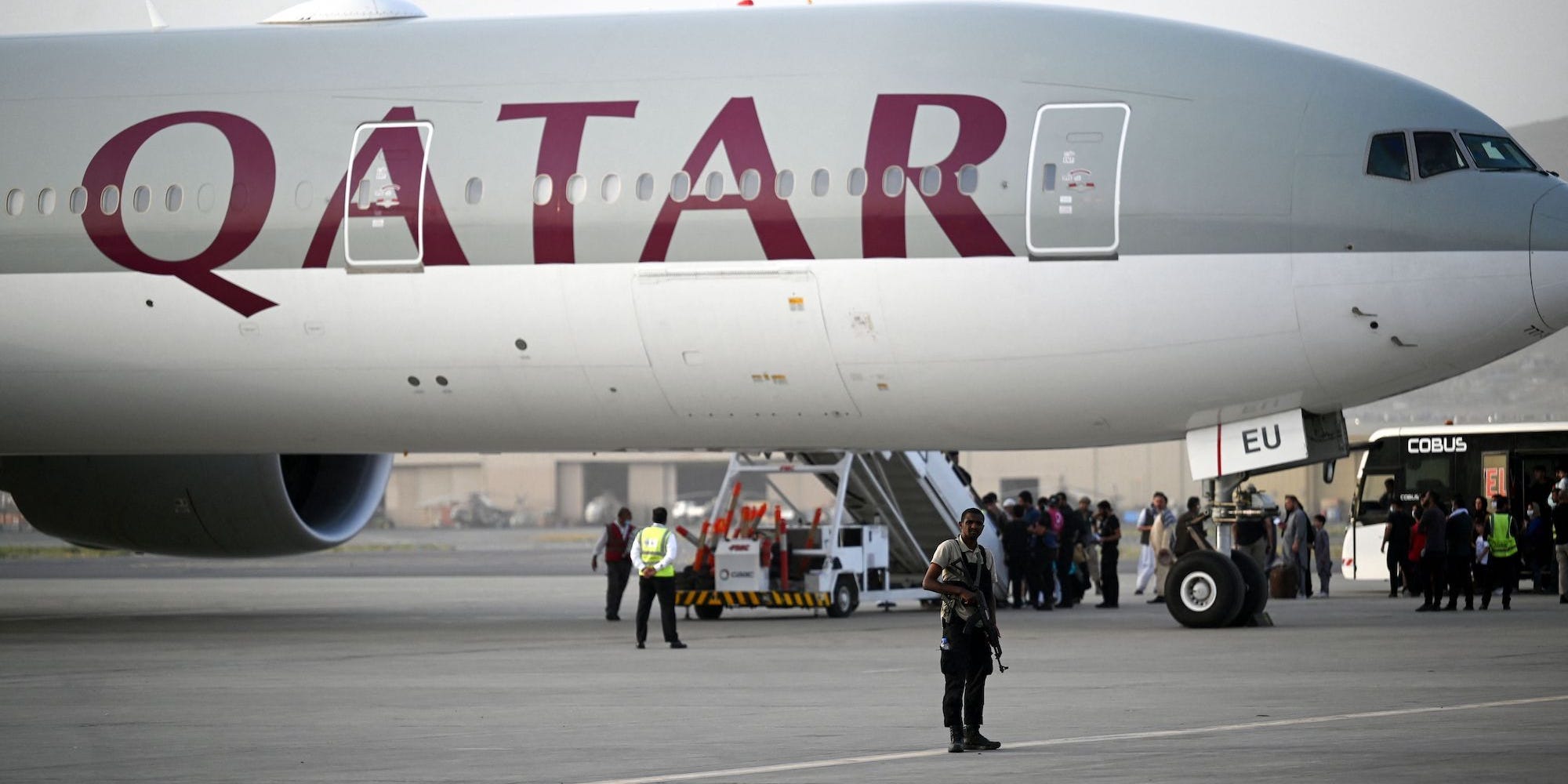 A Qatari security personnel stands guard (front) as passengers board a Qatar Airways aircraft bound to Qatar at the airport in Kabul on September 10, 2021.