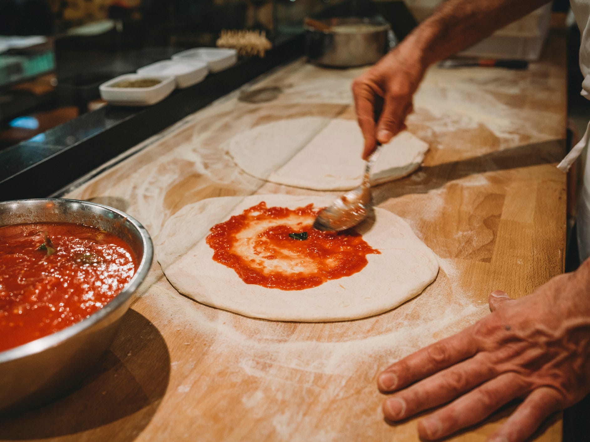 Someone spreading pizza sauce on pizza dough.