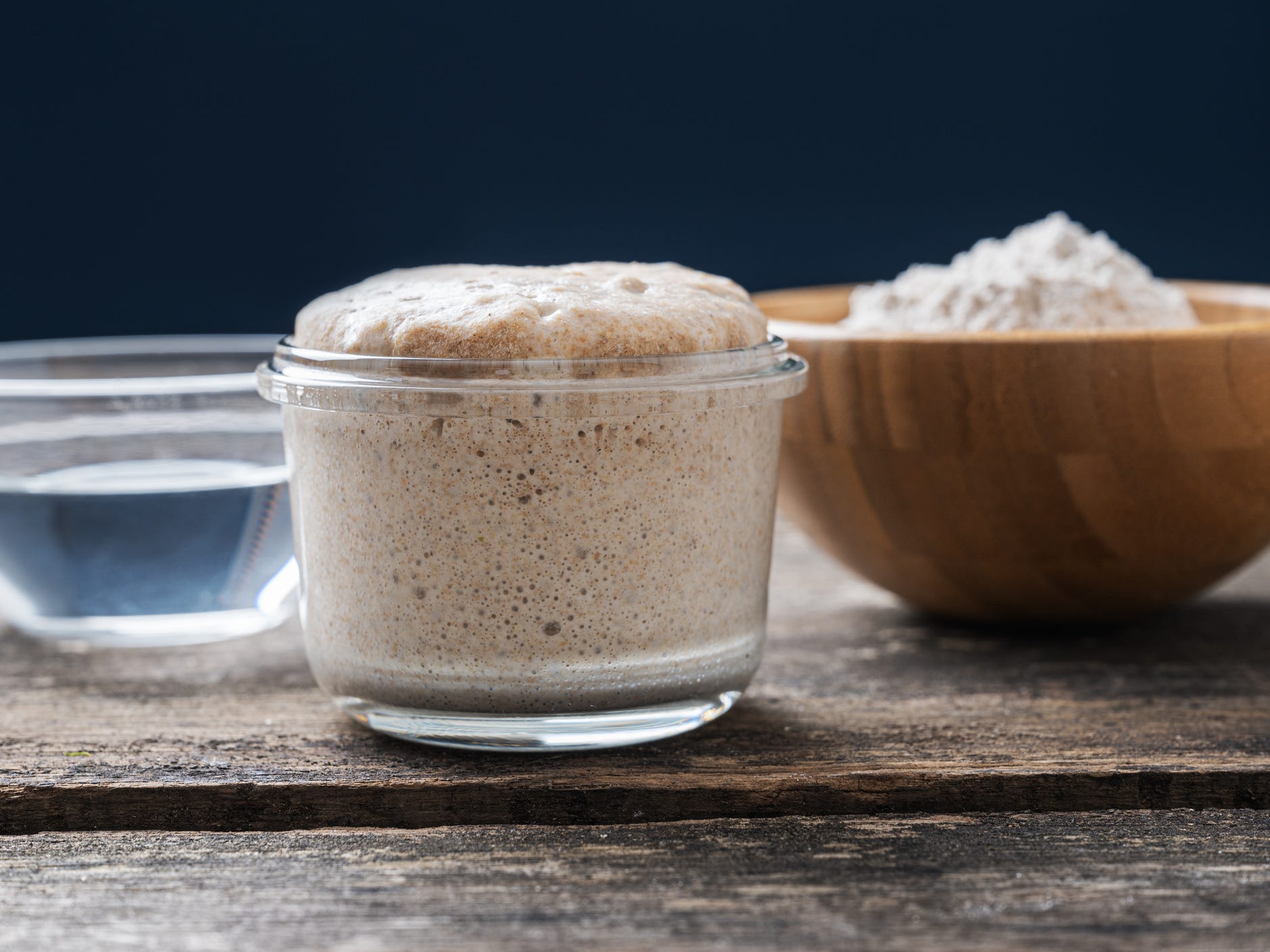 Sourdough starter in a clear jar in between a bowl of water and a bowl of flour.