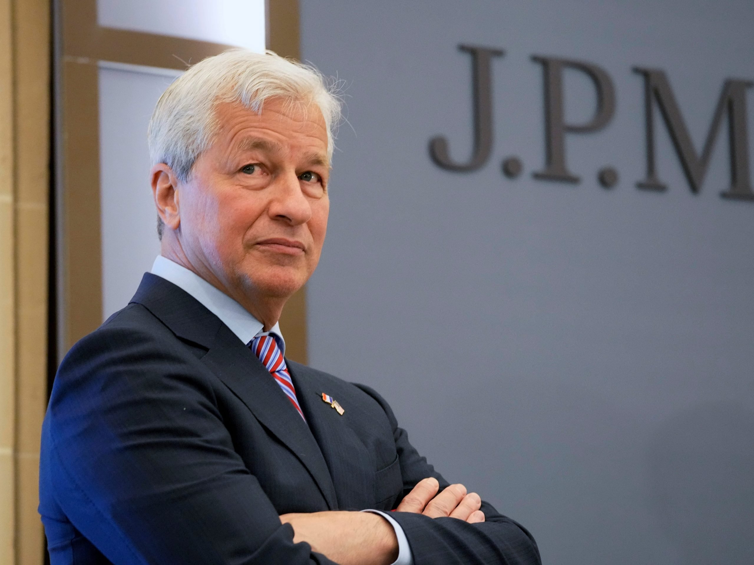 JPMorgan CEO Jamie Dimon crossing his arms in front of a JPMorgan sign