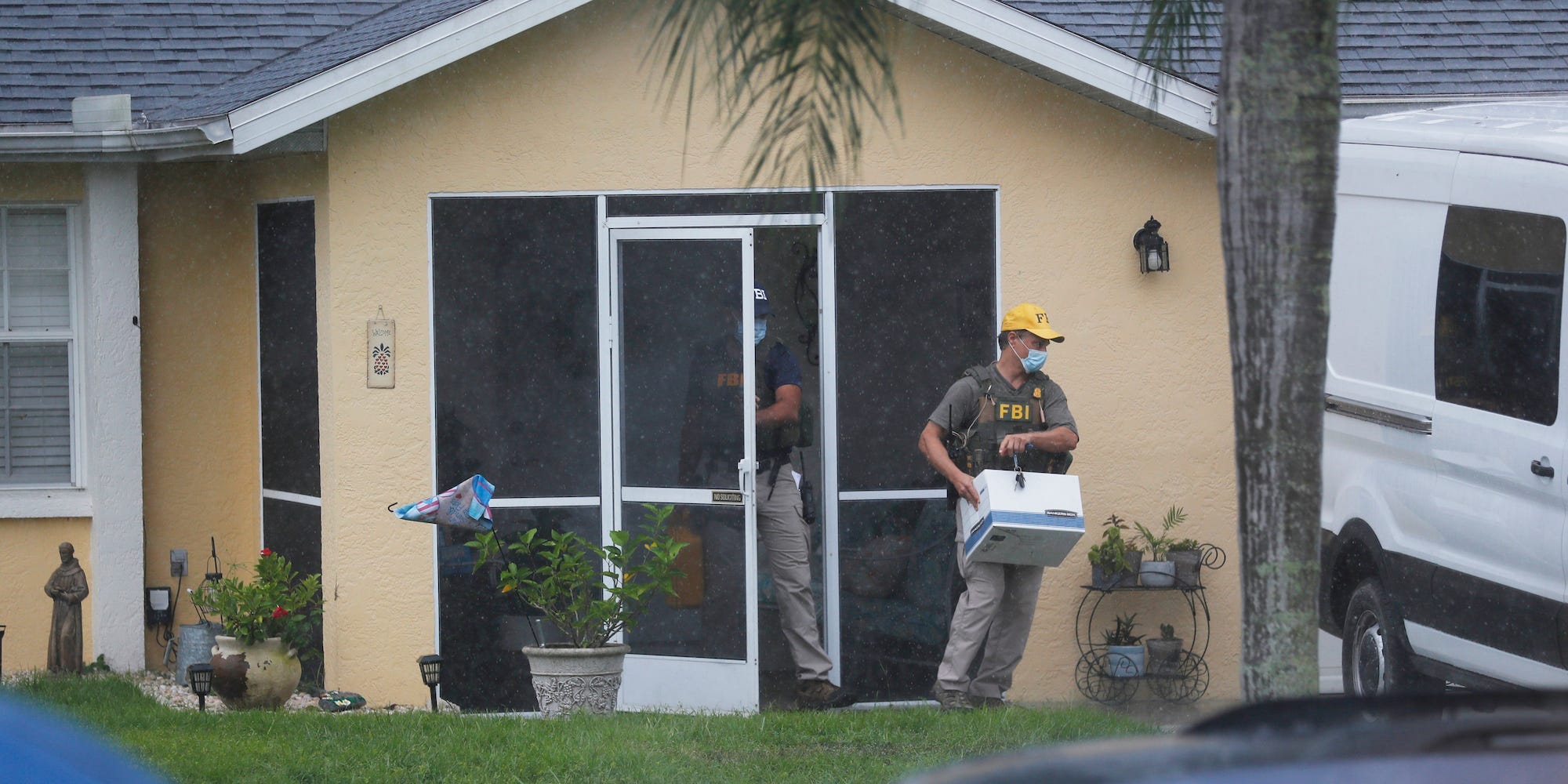 An FBI agent walks out of the door of the house with a box