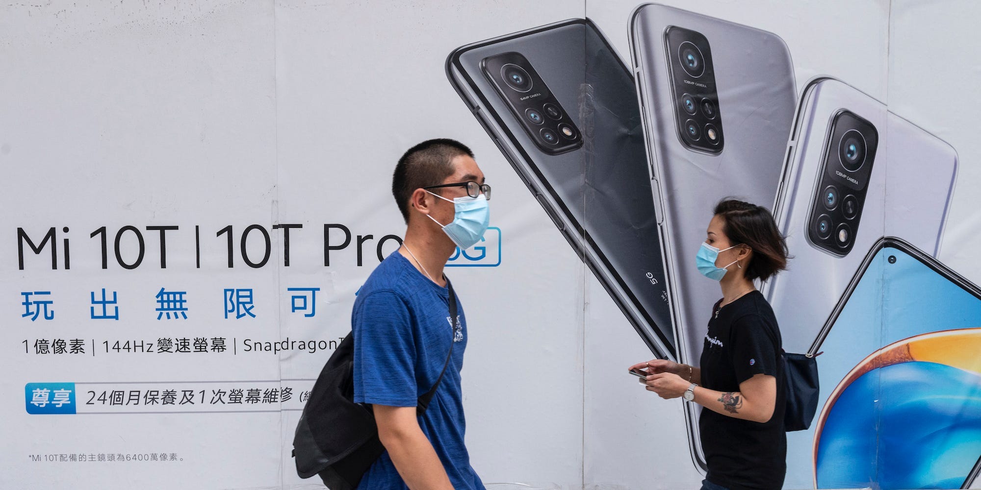 Commuters wearing face masks walk past the Xiaomi Mi 10T Pro 5G smartphone advertisement