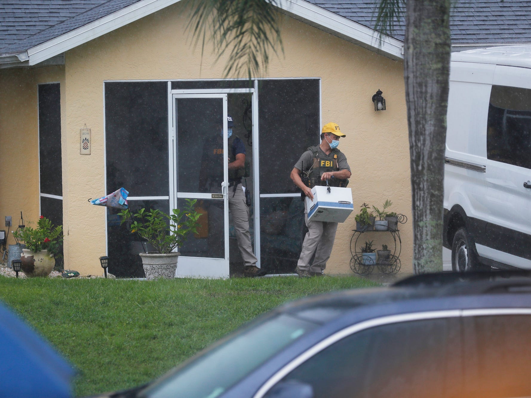 An FBI agent walks out of the door of the house with a box