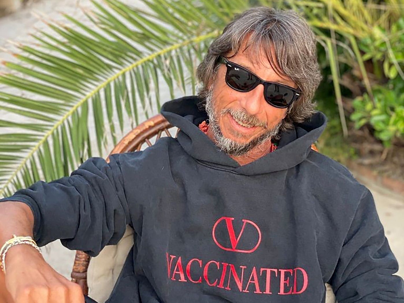 Valentino creative director Pierpaolo Piccioli wearing "Vaccinated" hoodie on beach in front of palm trees