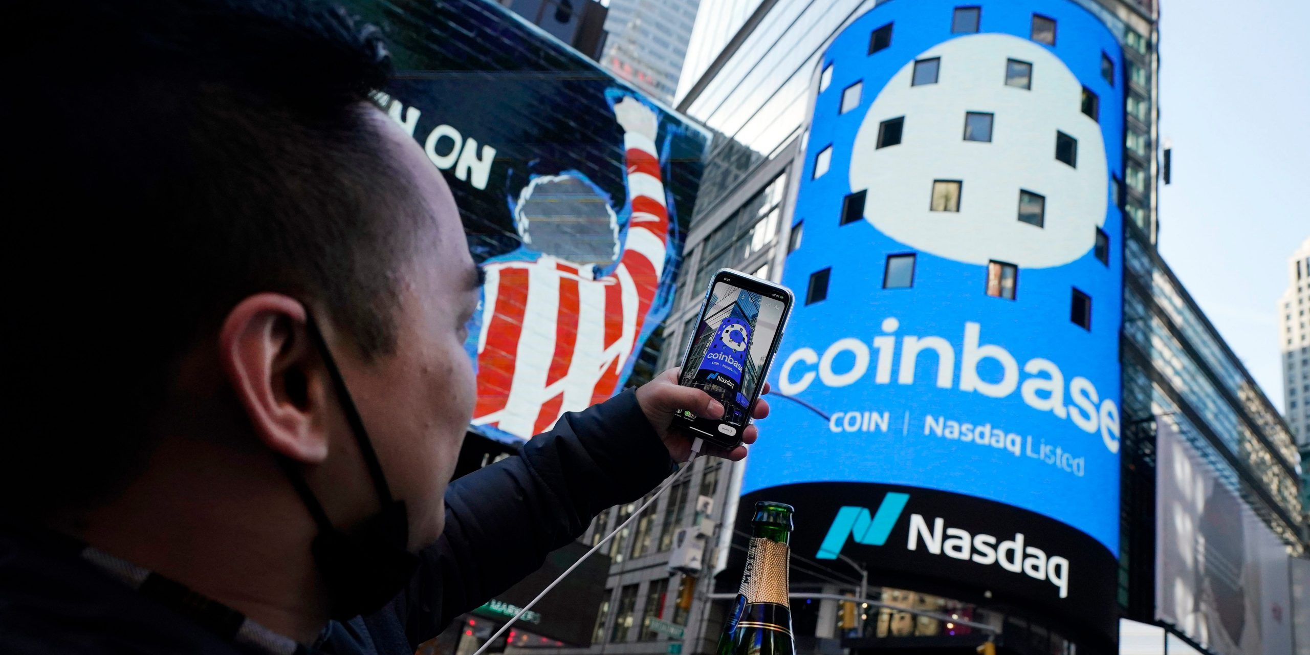 Coinbase employee Daniel Huynh holds a celebratory bottle of champagne as he photographs outside the Nasdaq MarketSite, in New York's Times Square, Wednesday, April 14, 2021.