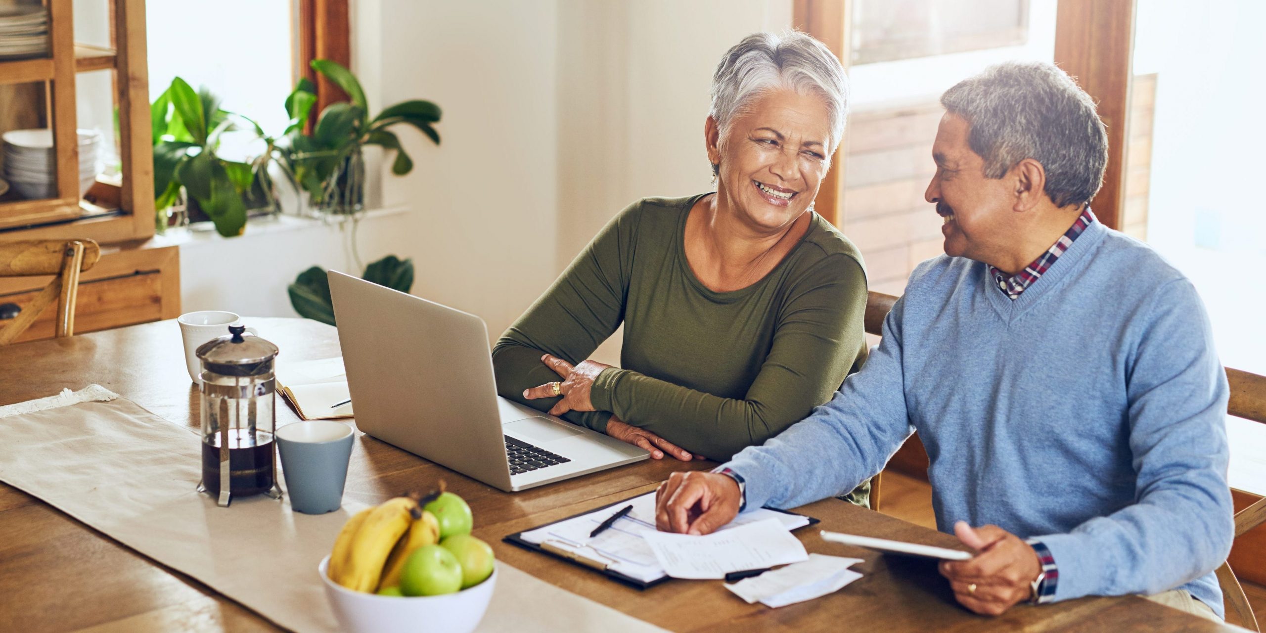 Two people smiling at each other while sitting at a desk with a computer and papers.