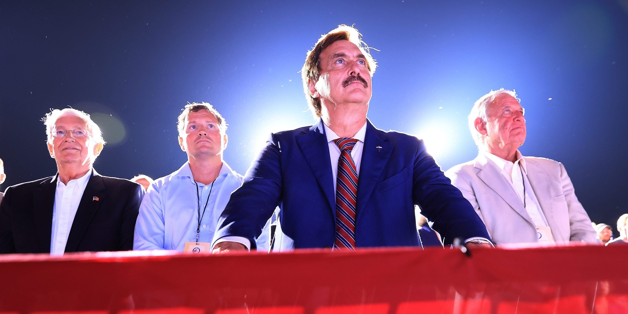 Mike Lindell standing behind a red barricade at a Trump rally.