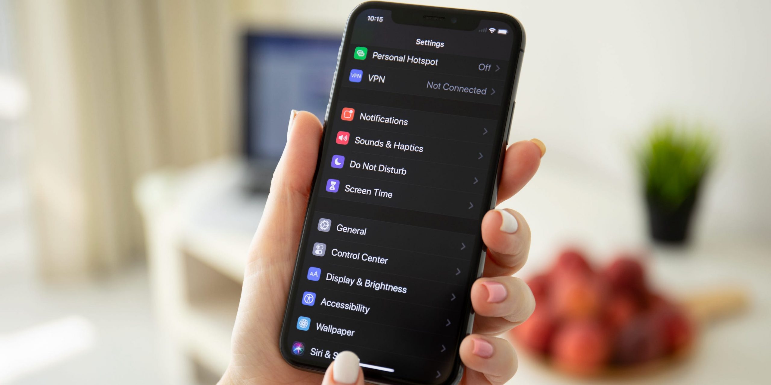 A person holding an iPhone. The iPhone is in Dark Mode, and the Settings app is opened.