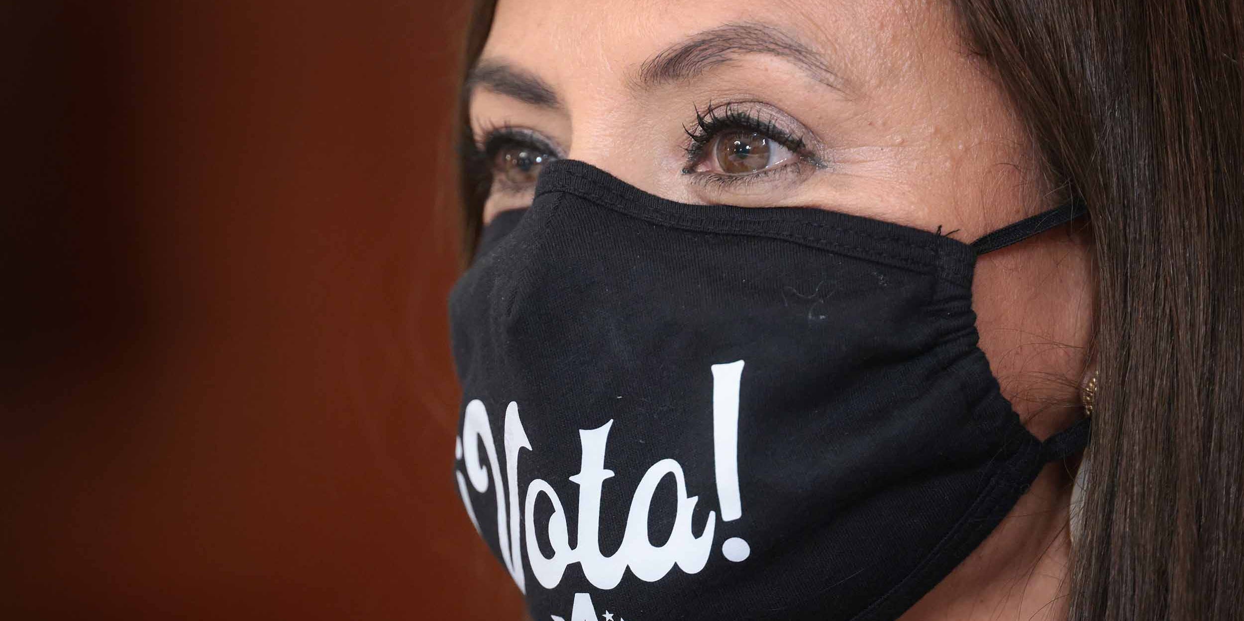 A voter is seen wearing a face covering with the Spanish translation of the word "vote" written on it.