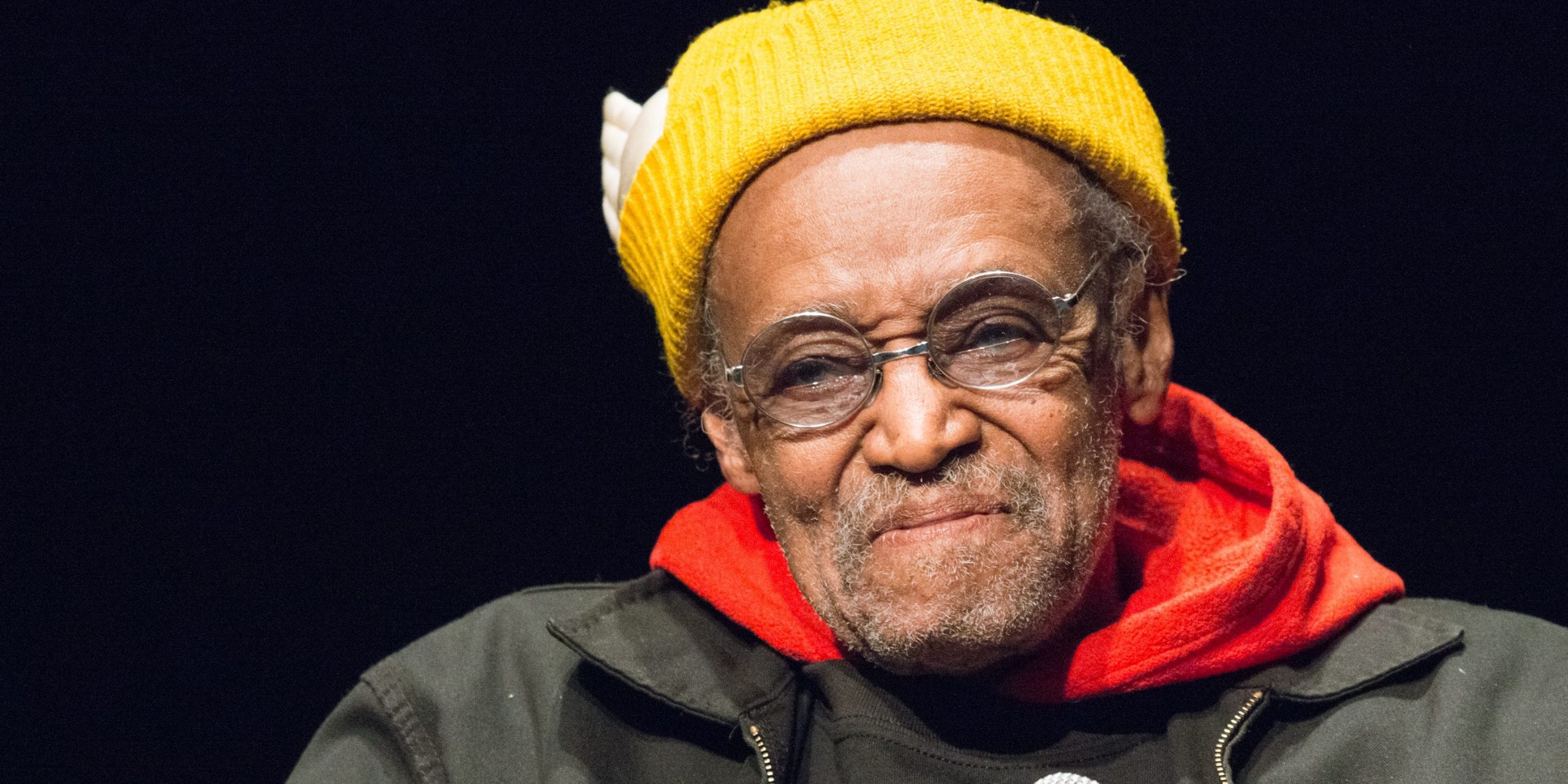 Melvin Van Peebles smiling and holding a microphone