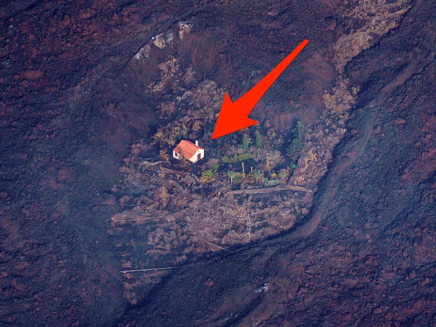 an arrow points to a house surrounded by earth scorched by the lava from the Cumbre Vieja violcano eruption on La Palma island