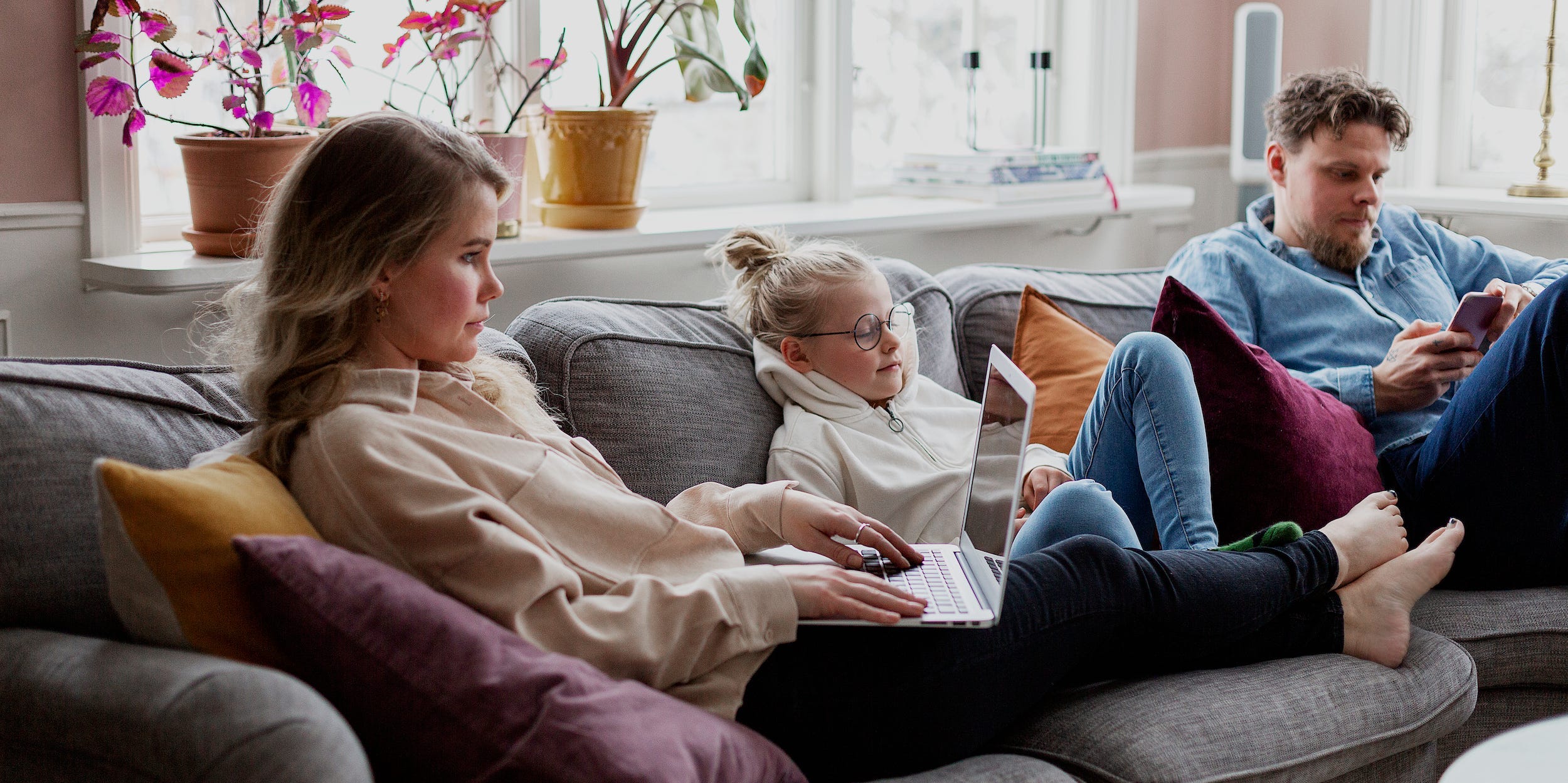 family sitting on couch using laptops and phones