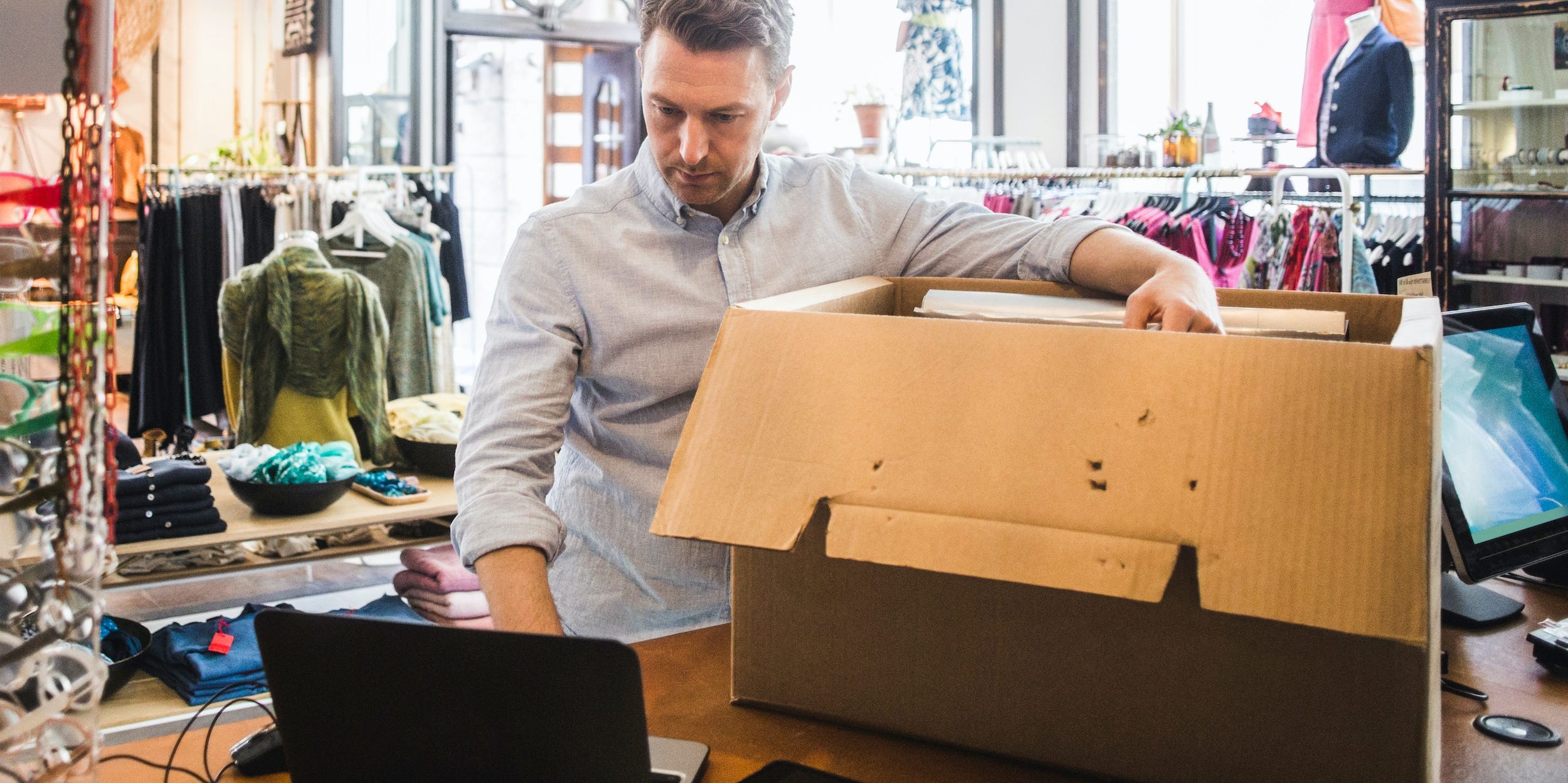 business owner looking at laptop shipping a box in clothing store