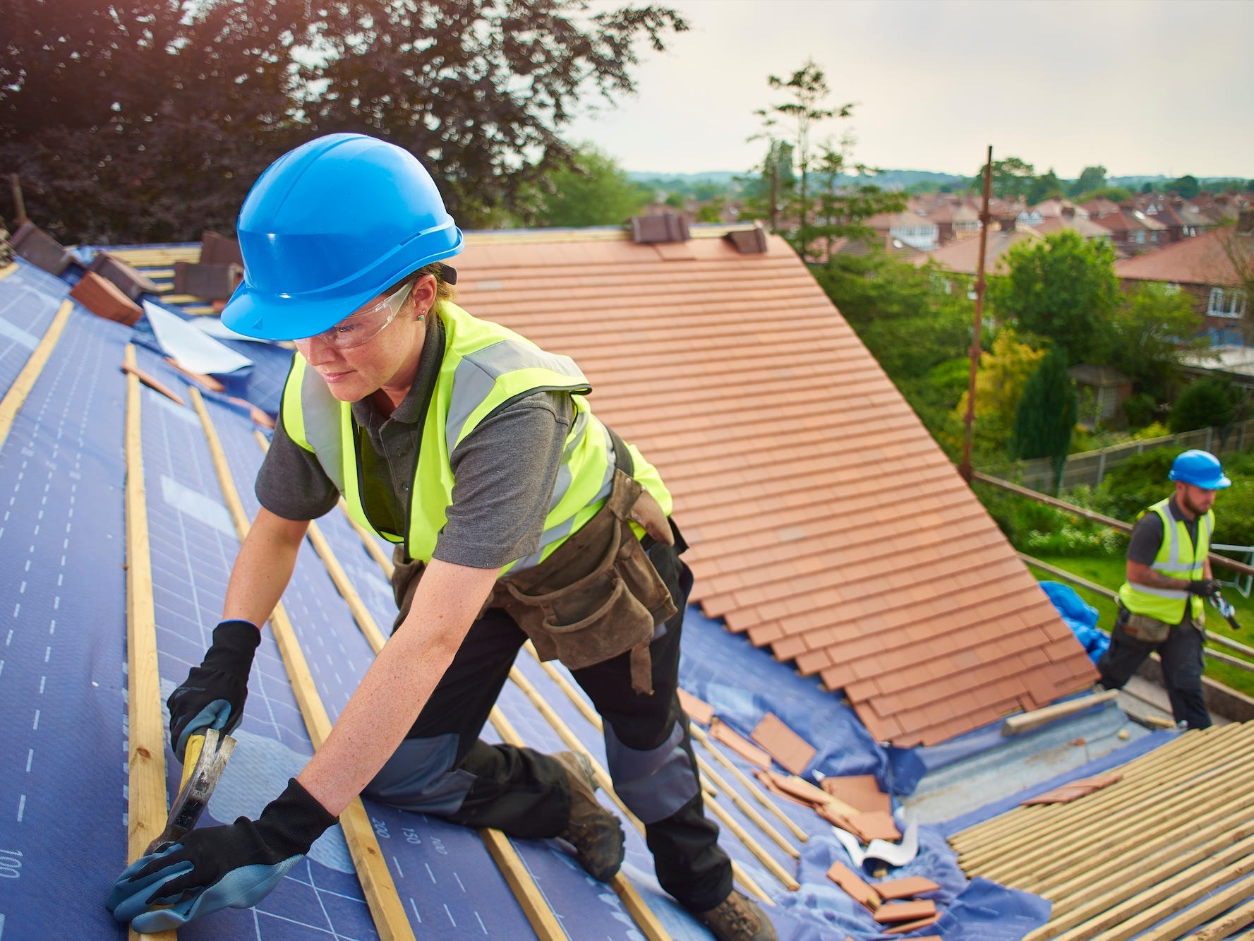 roofer nails on roof tiles with her colleague in the background