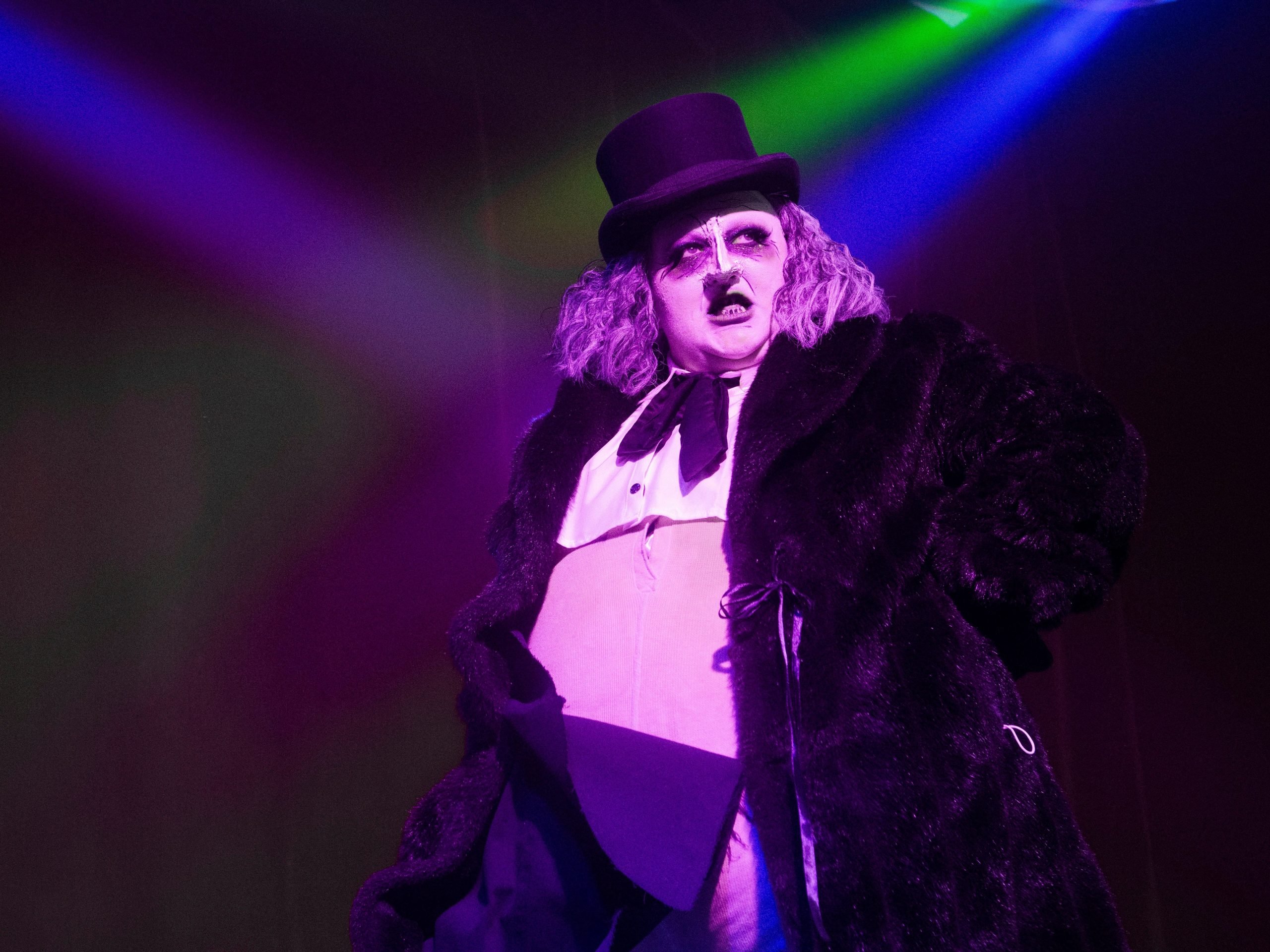 A performer wears a top-hat with colorful lights in the background.